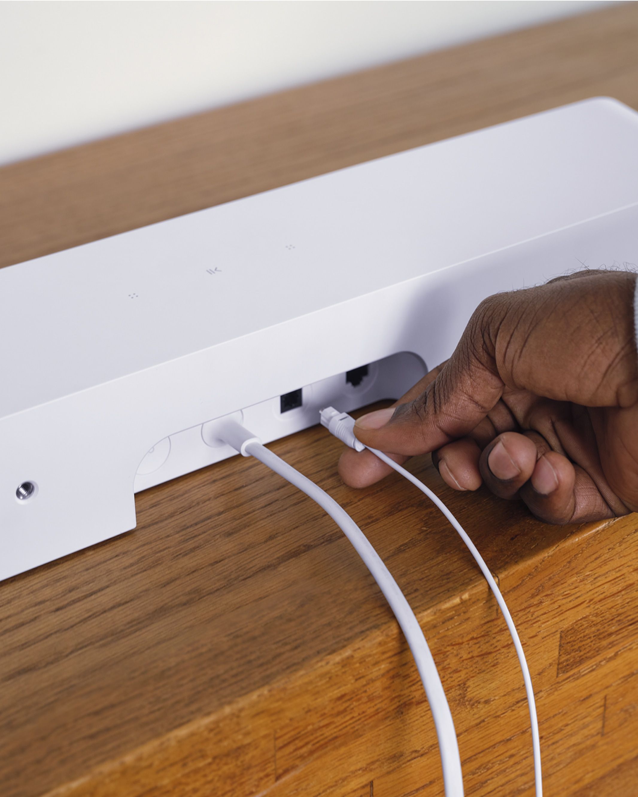 Detail zadní strany bílého Sonos Ray, ruka zapojuje optický a síťový kabel