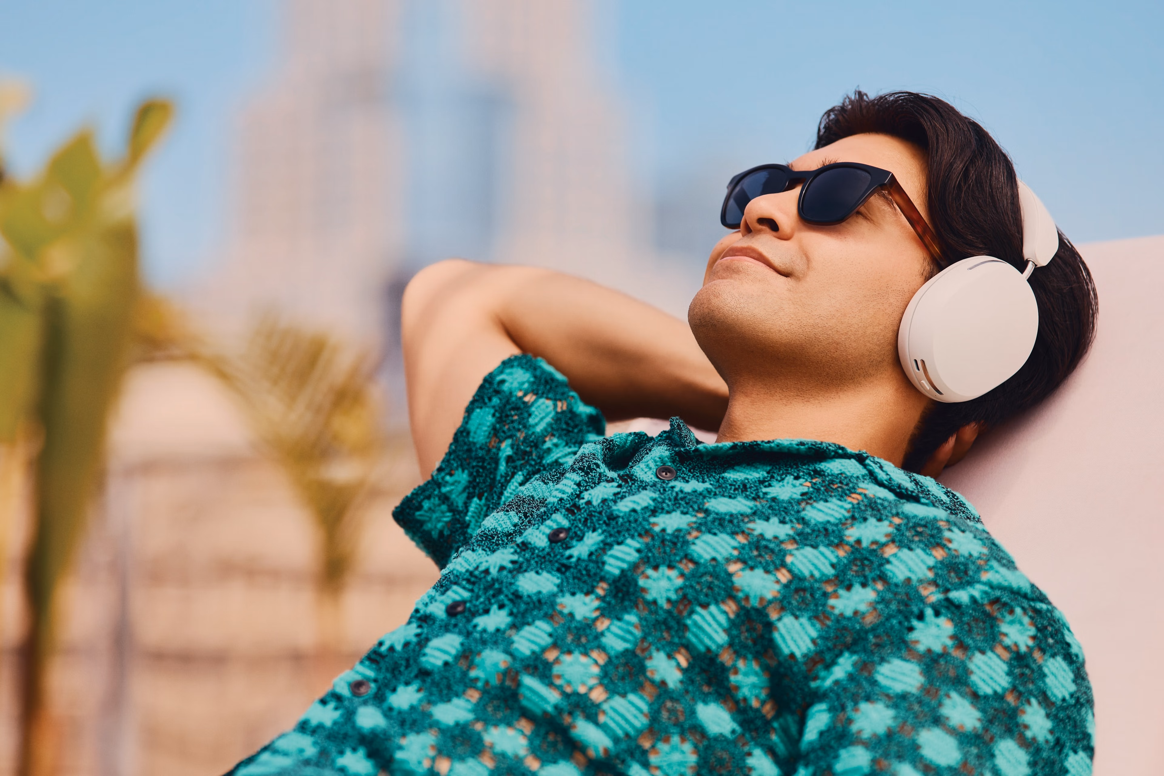 Person wearing a pair of Soft White Sonos Ace headphones while lounging on a chair outside