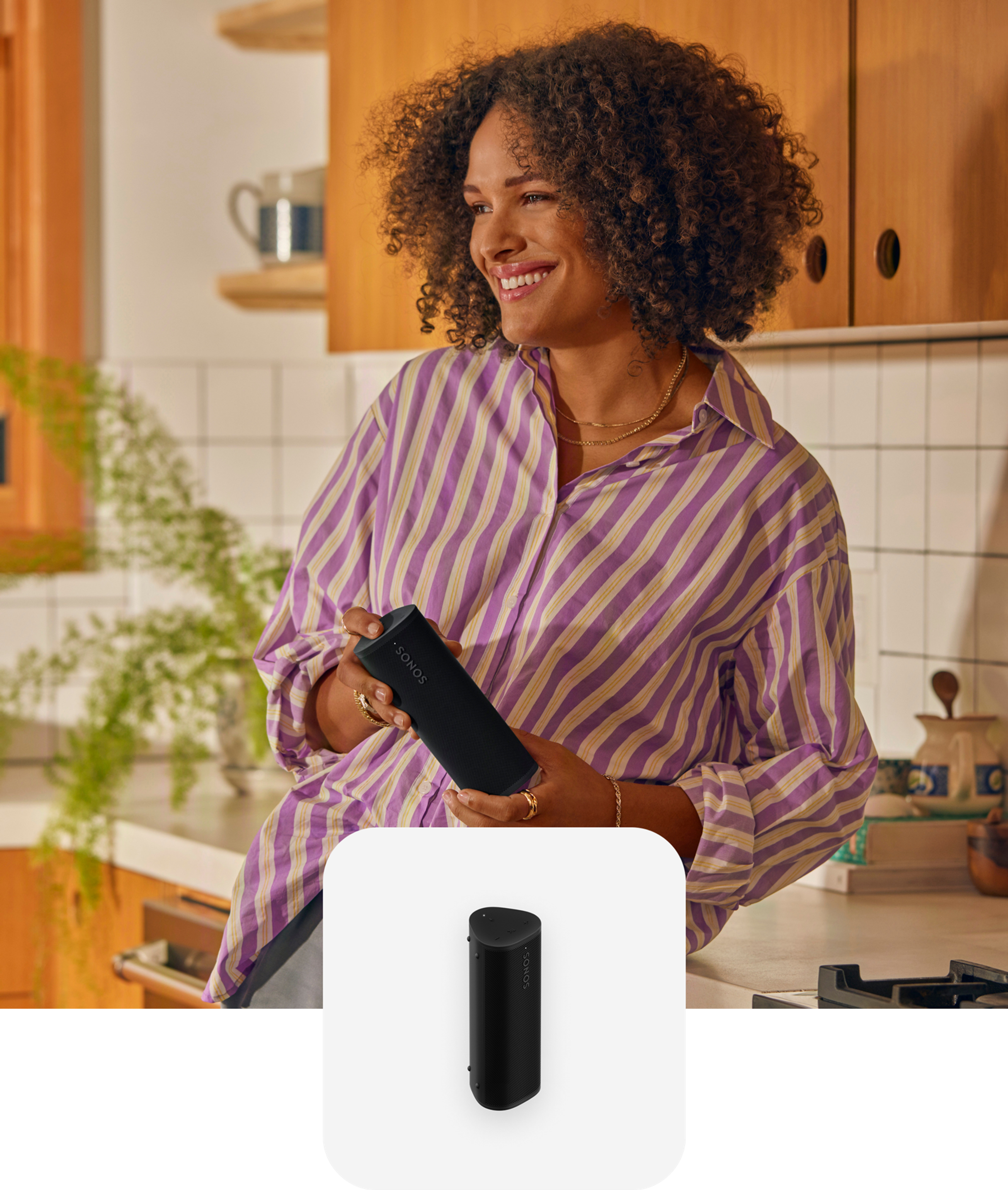 Woman holding a black Roam 2 portable speaker listening to music in the kitchen