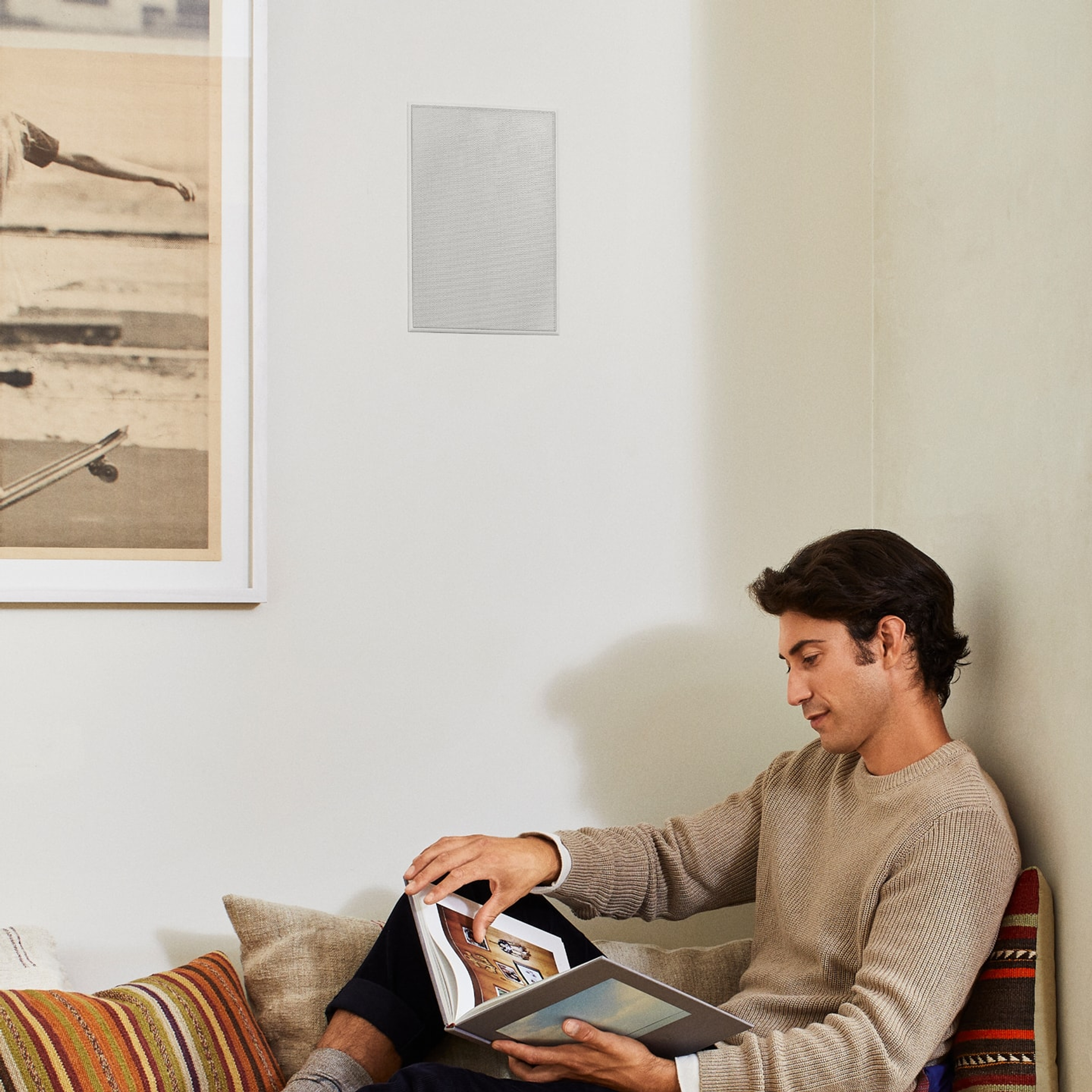 Person sitting next to Sonos in-wall speaker reading a book