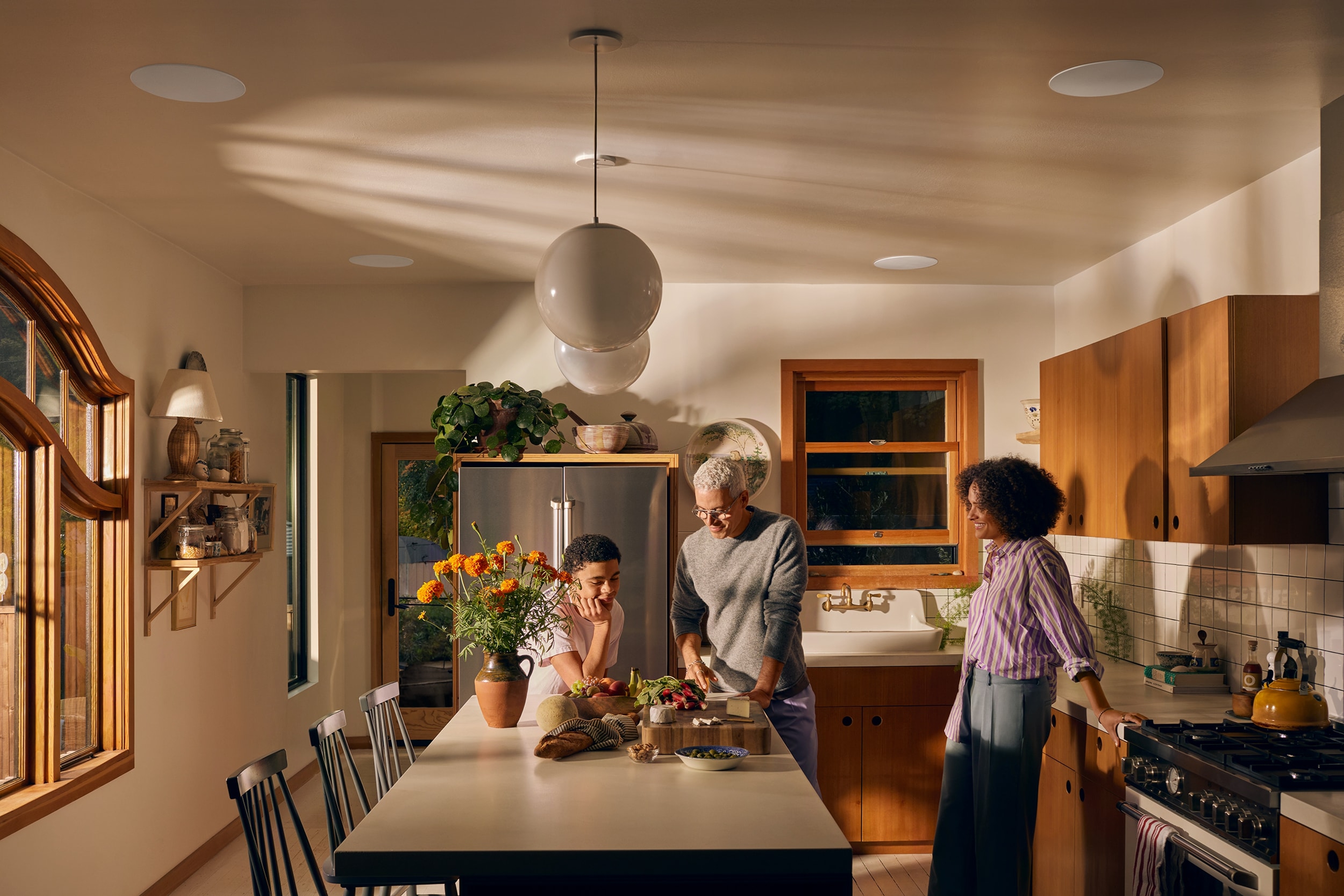 Family in the kitchen with Sonance in-ceiling speakers installed over an island