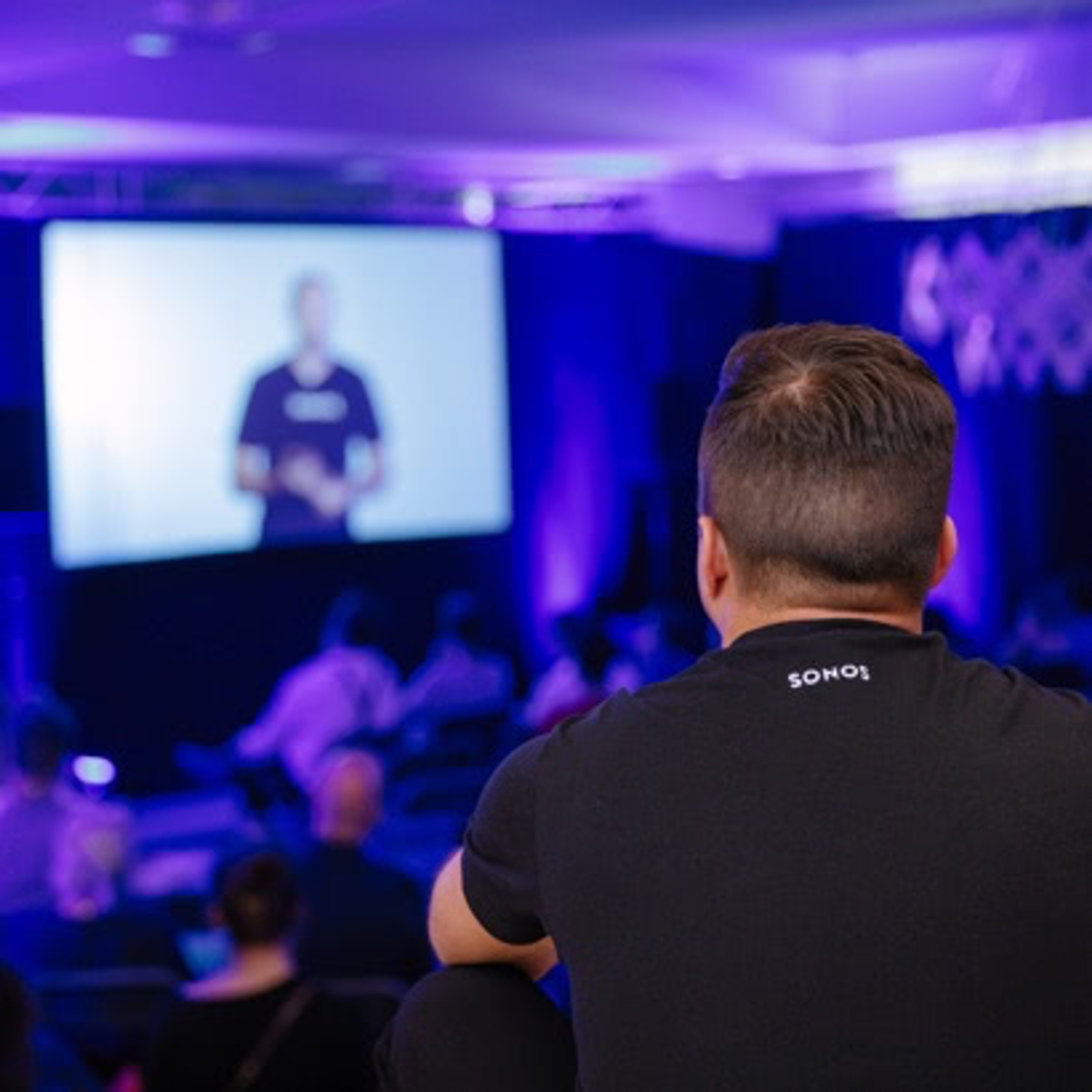 The back of a person's head at a conference listening and watching a video