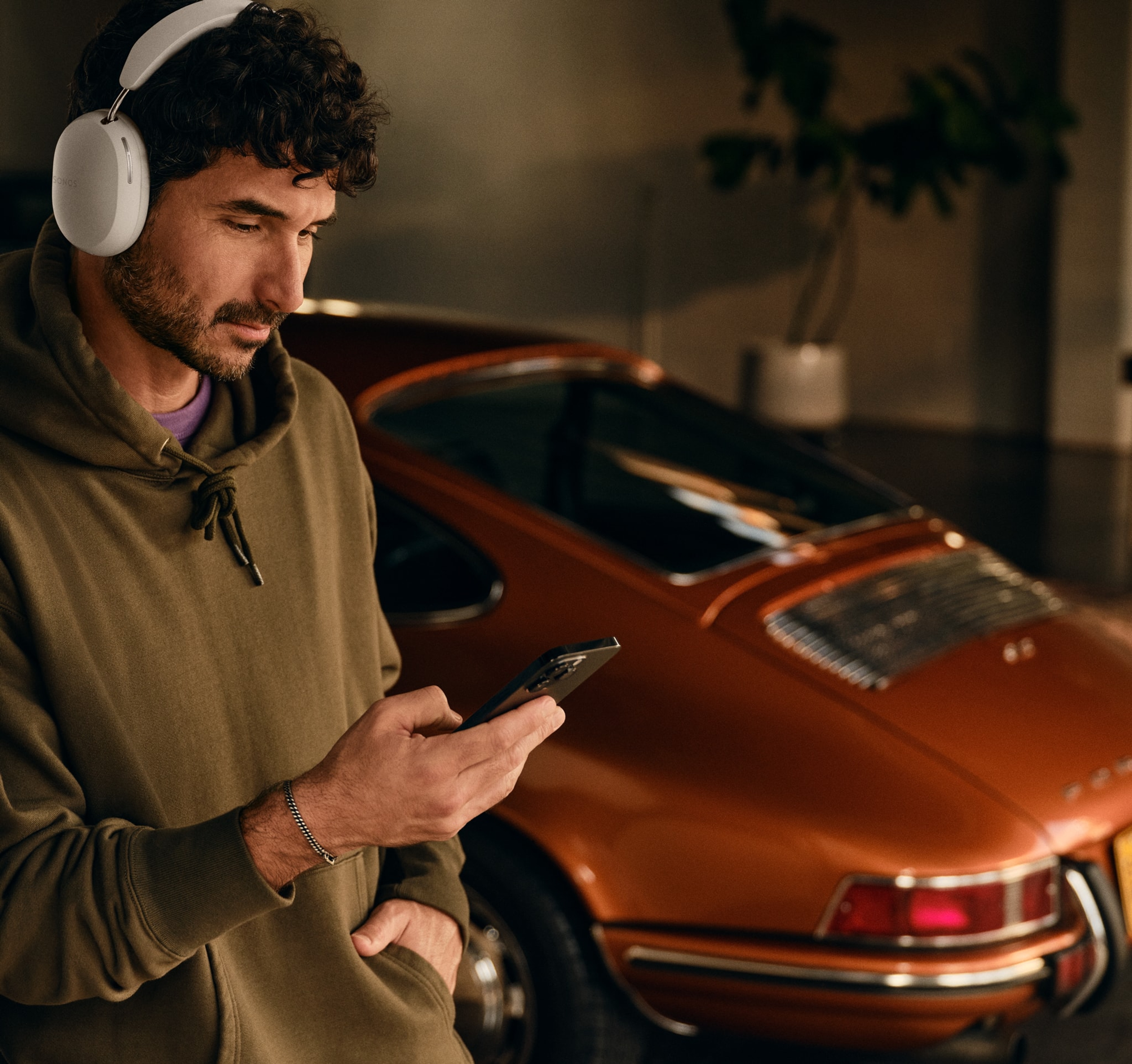 Person wearing white Sonos Ace and using his phone next to a car