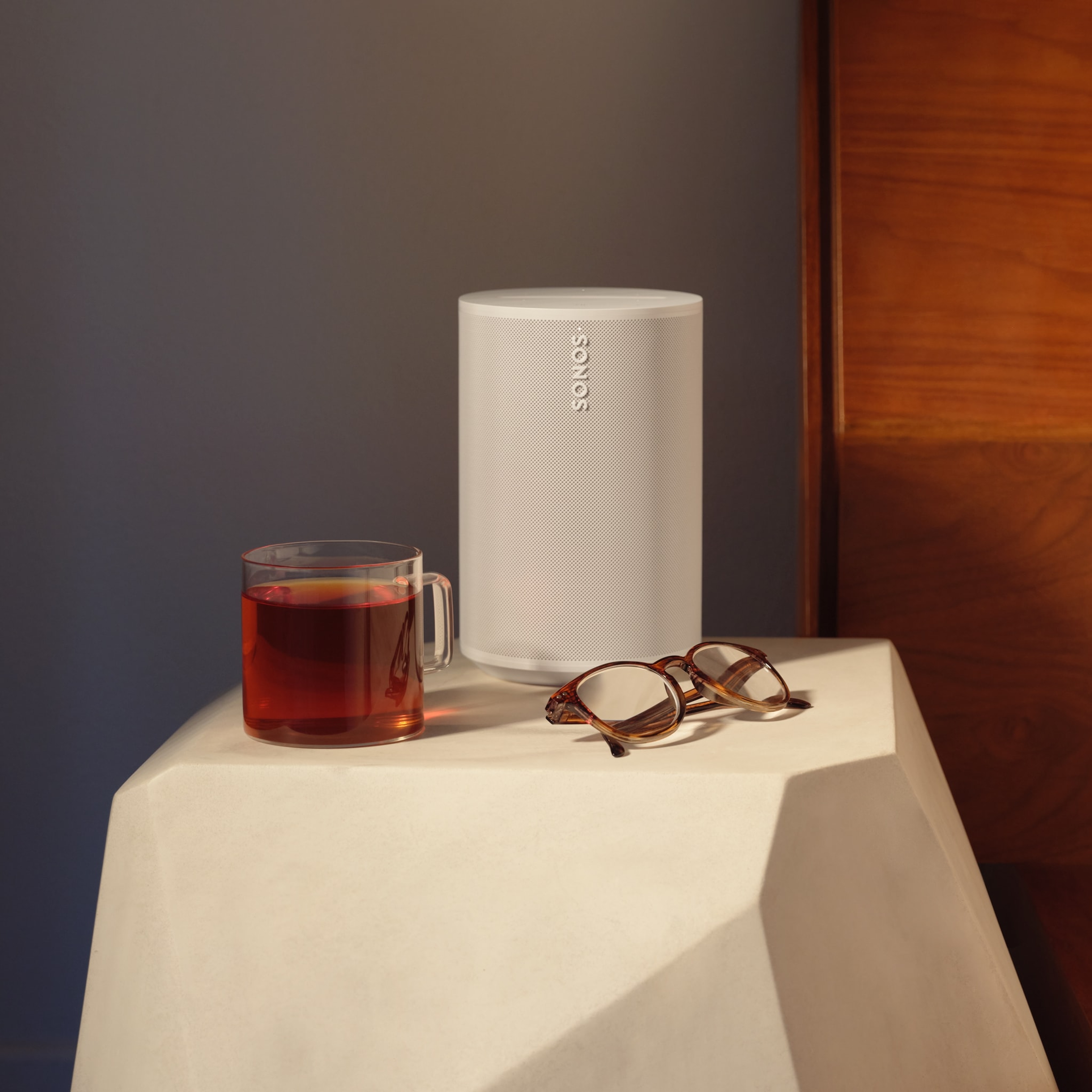 A white Era 100 speaker on a nightstand next to a bed