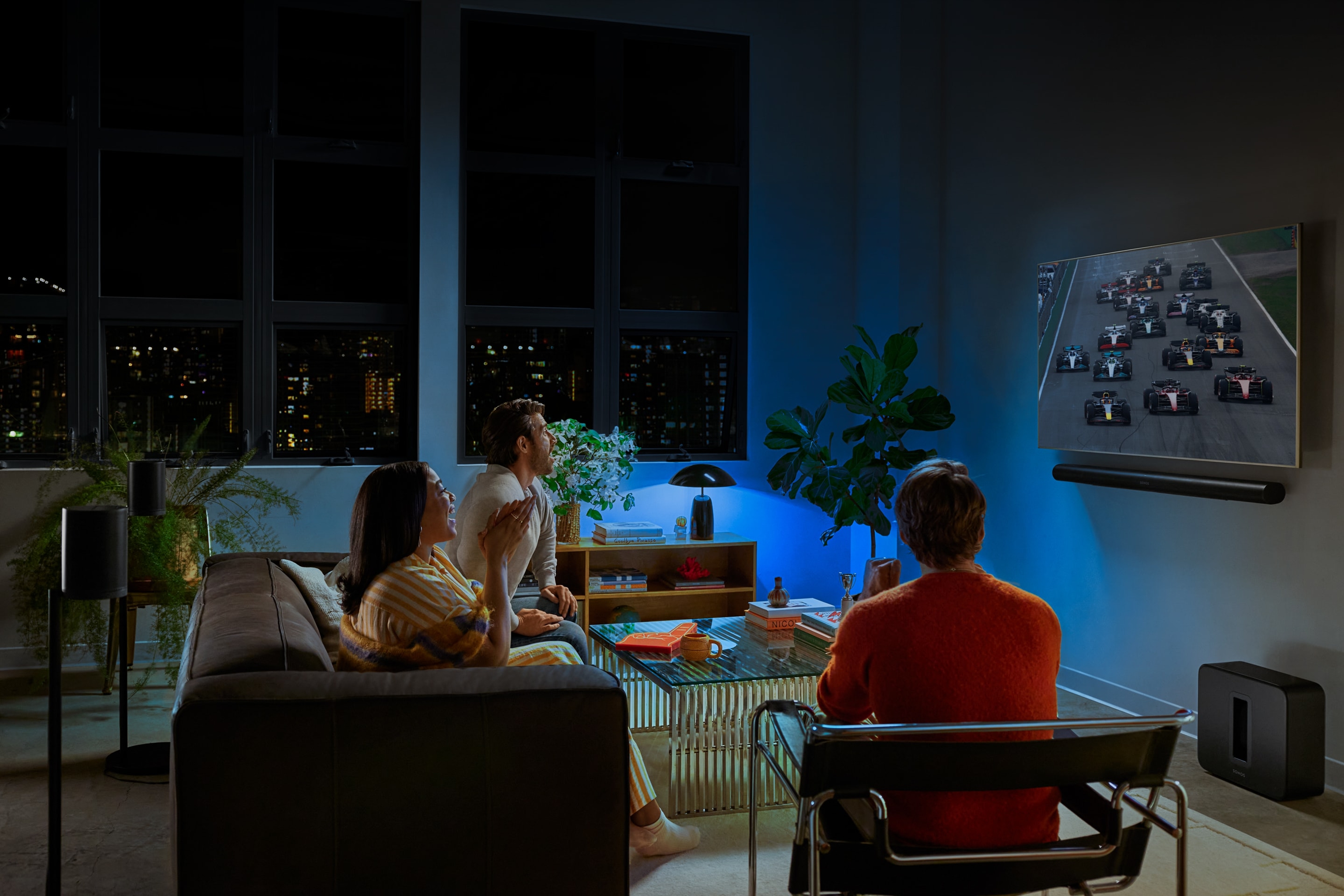 Group of three people watching F1 race on TV 