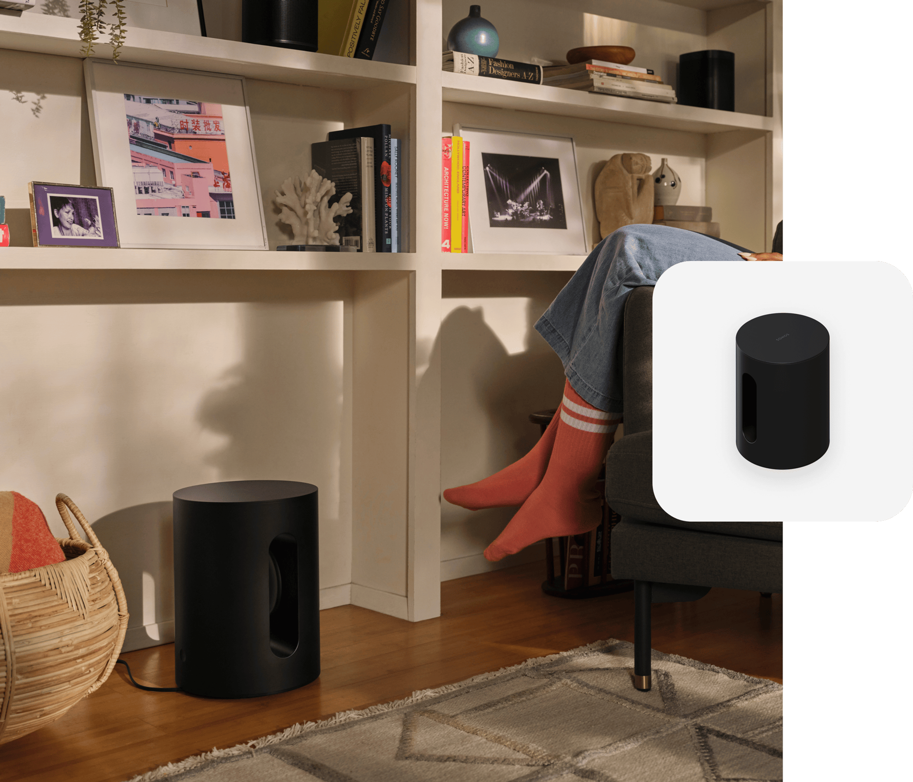 User sitting in living room armchair next to a black Sonos Sub Mini