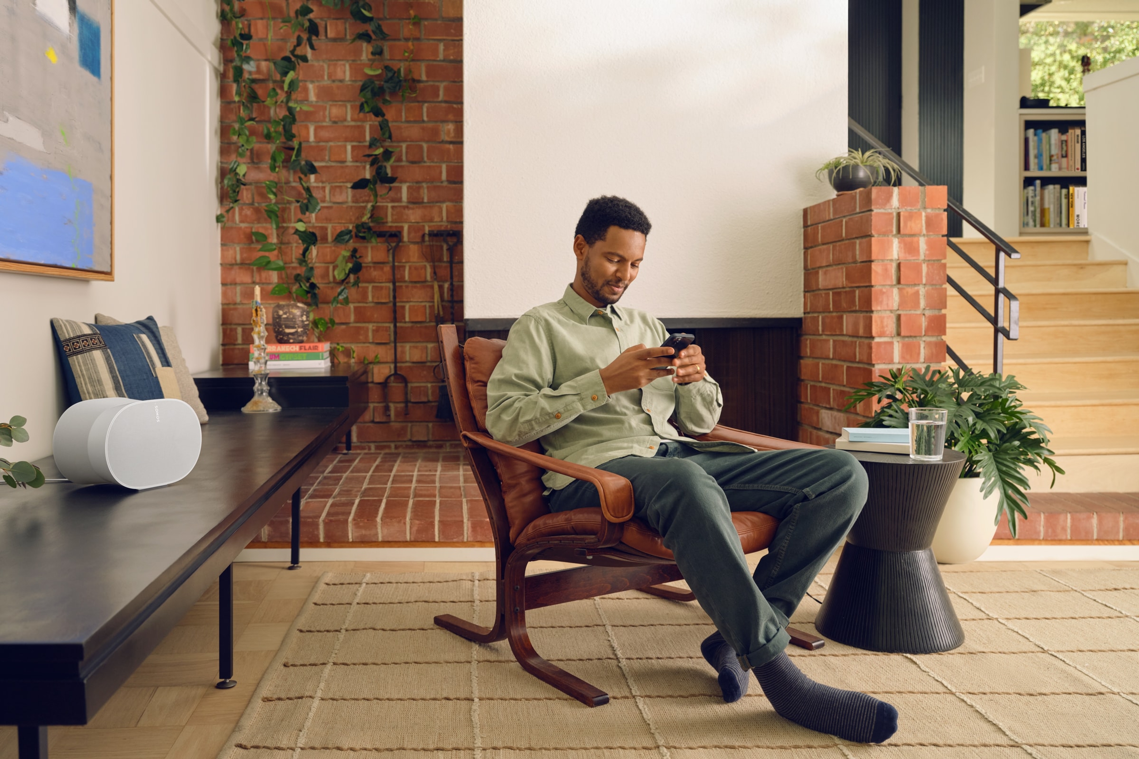 A user sitting in a chair controlling their white Sonos Era 300 speaker with the Sonos app