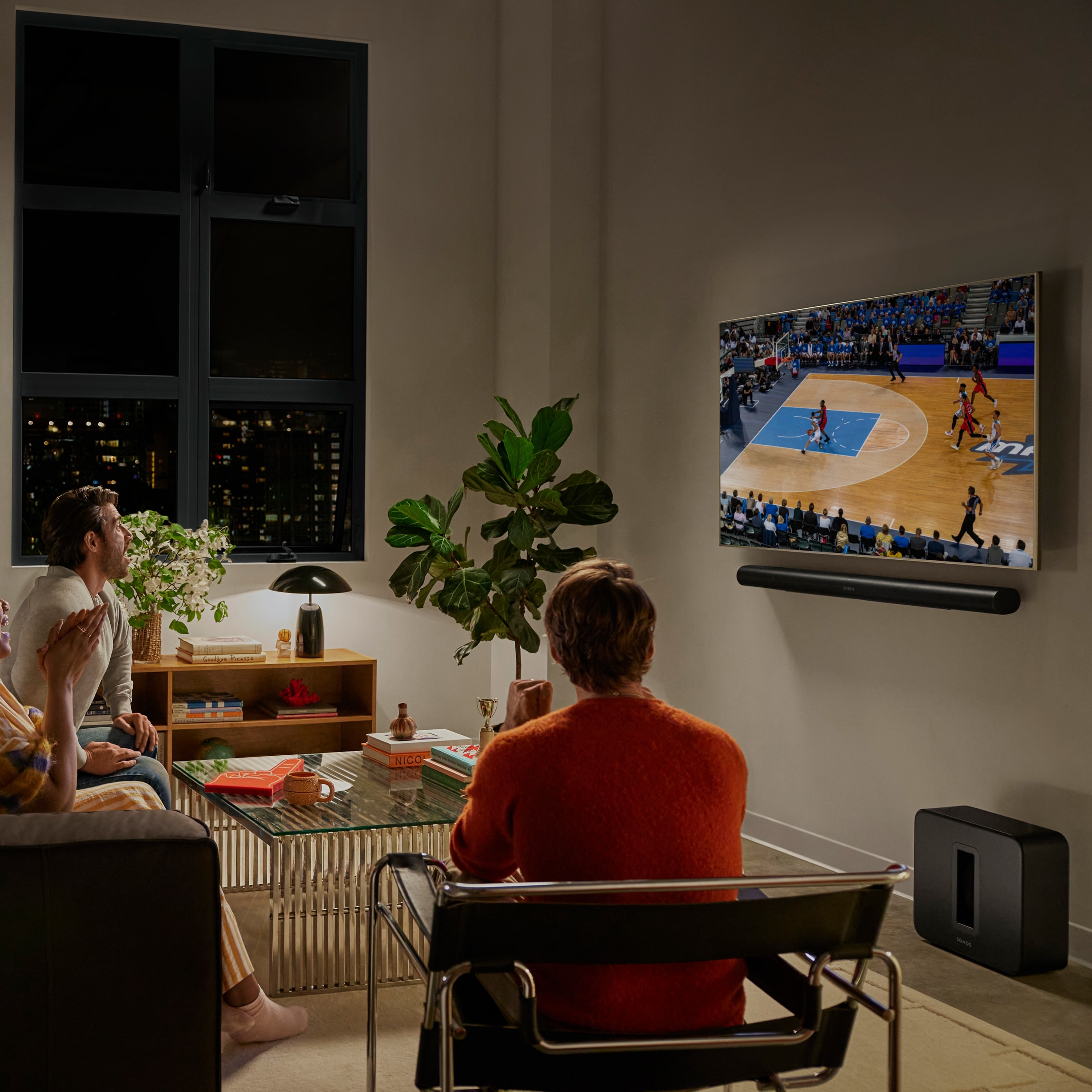A group of friends in a living room watching a basketball game with a black Arc Ultra and a black Sub 4