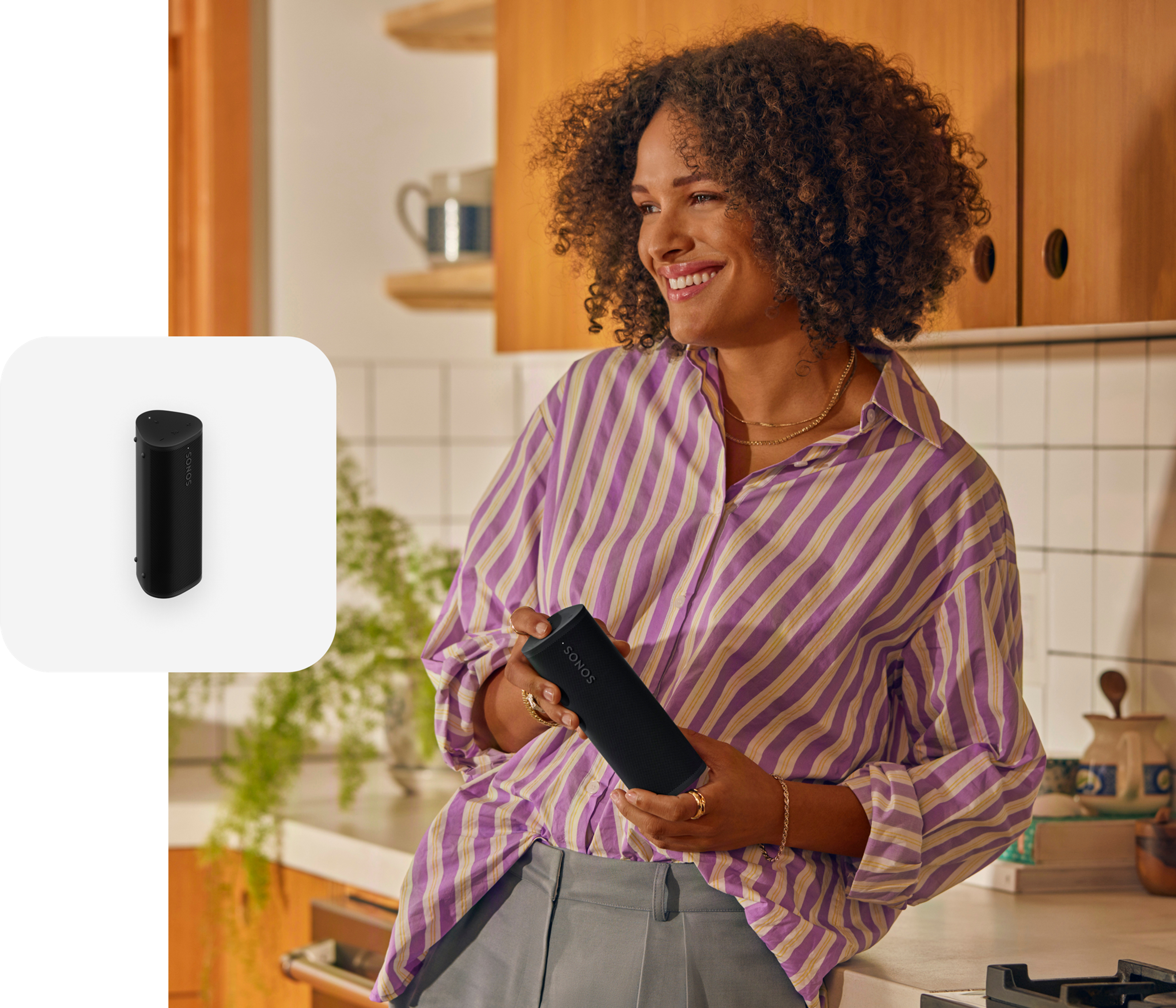 Woman holding a black Roam 2 portable speaker listening to music in the kitchen