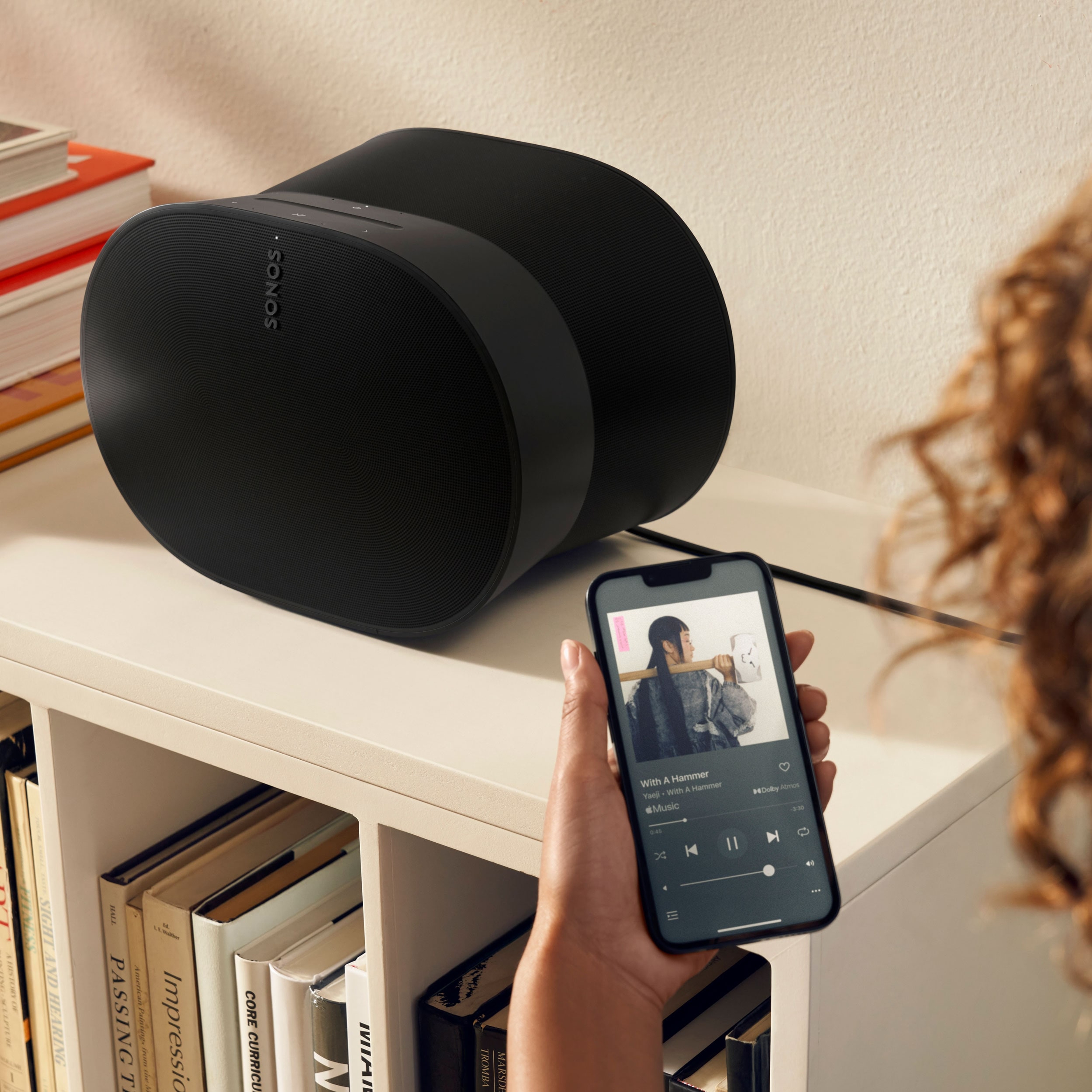 Woman using her phone to control a black Era 300 on a bookshelf
