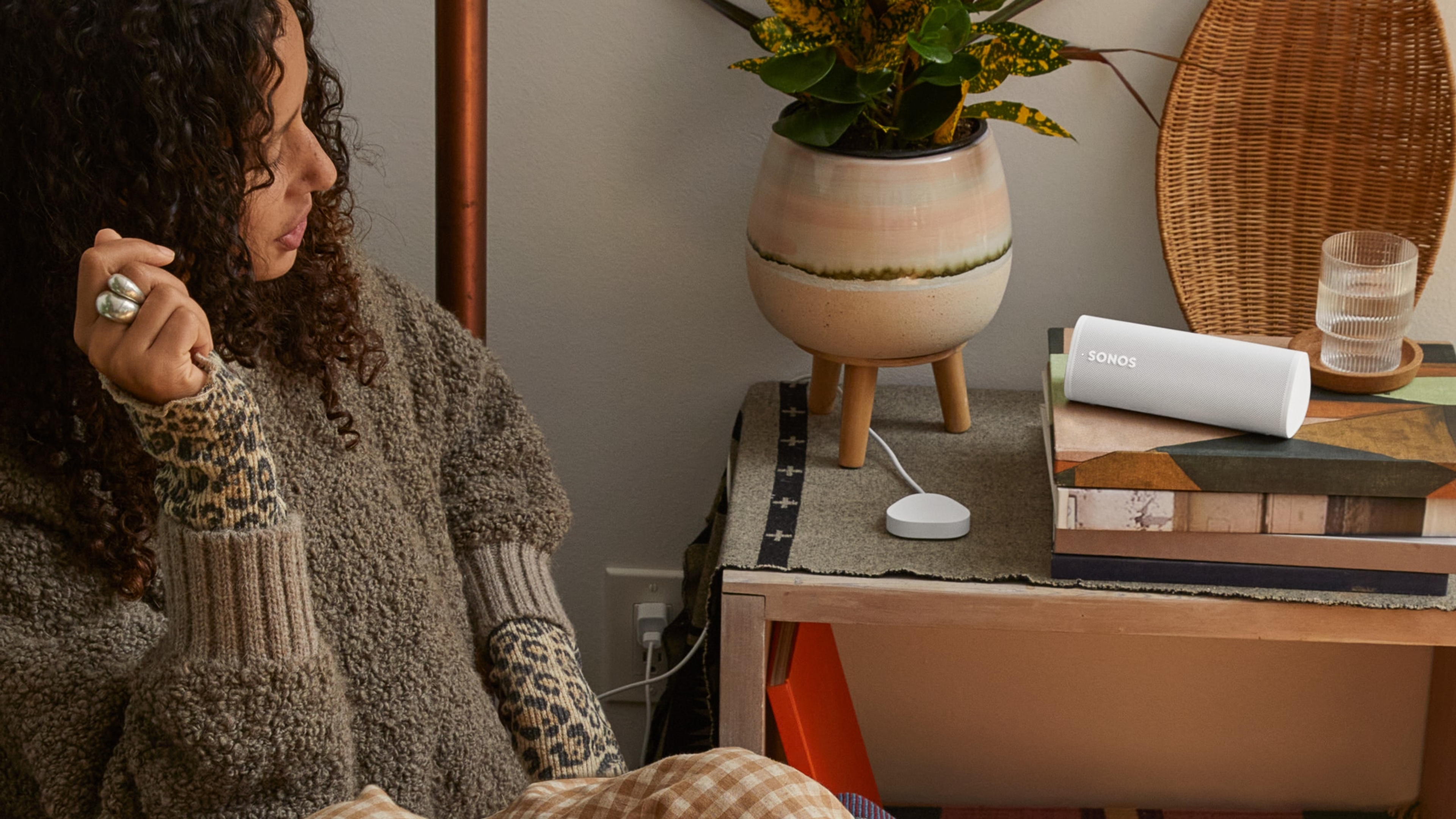 A woman in her bedroom with a white Roam 2 speaker on the nightstand