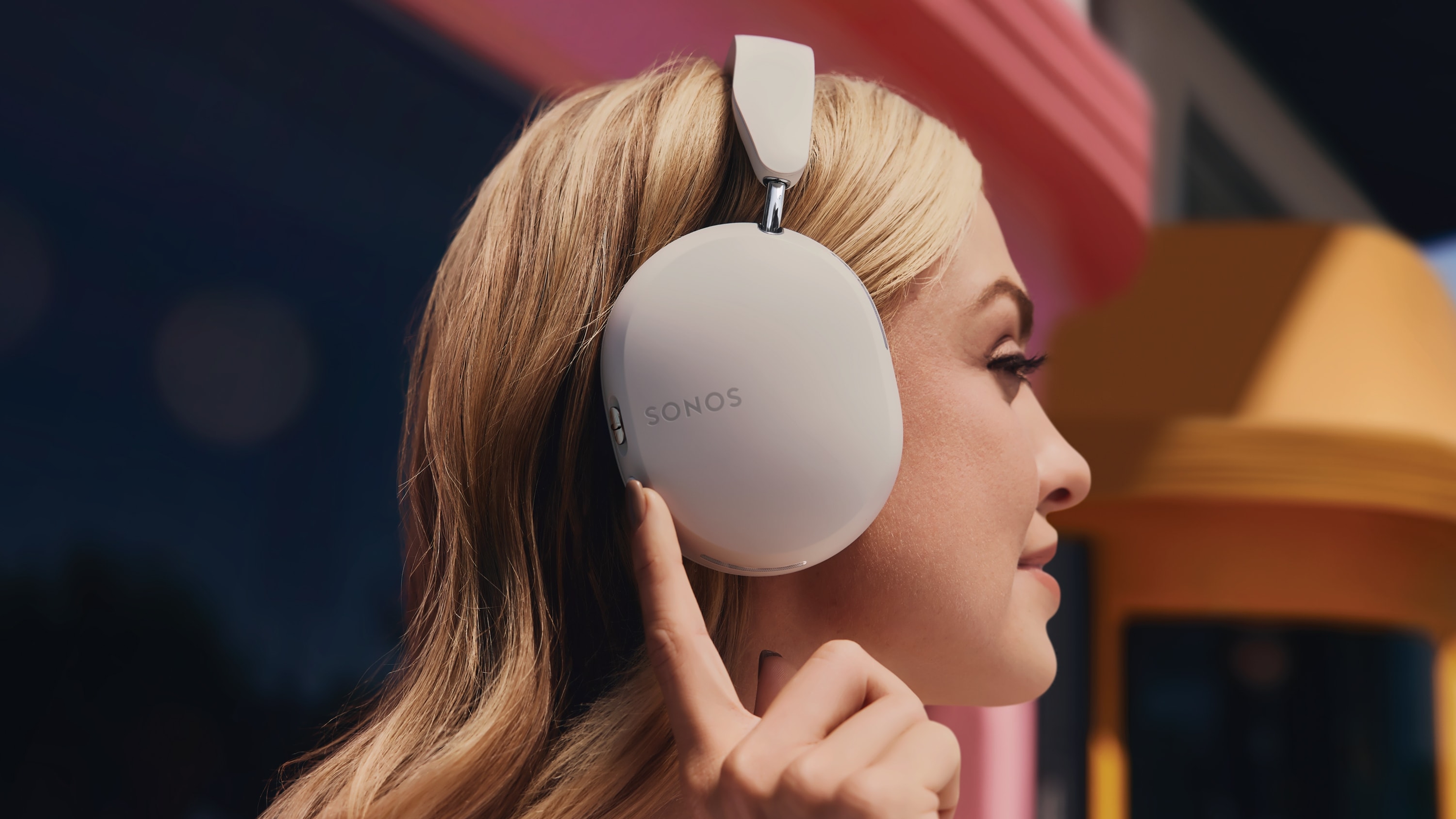 Side profile of a person wearing Soft White Sonos Ace headphones and pressing the active noise cancellation button 