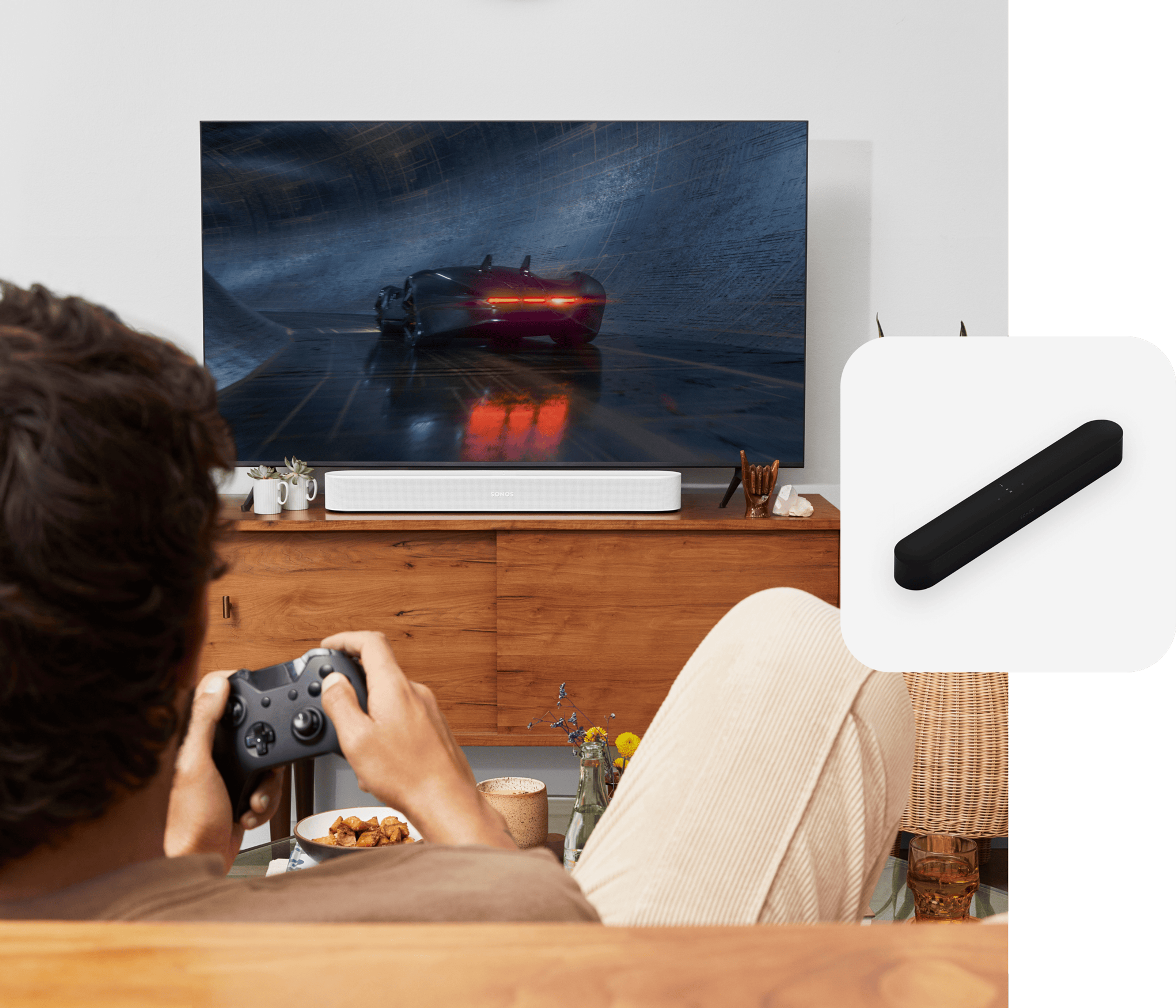 User sitting on couch gaming with a white Sonos Beam soundbar for audio