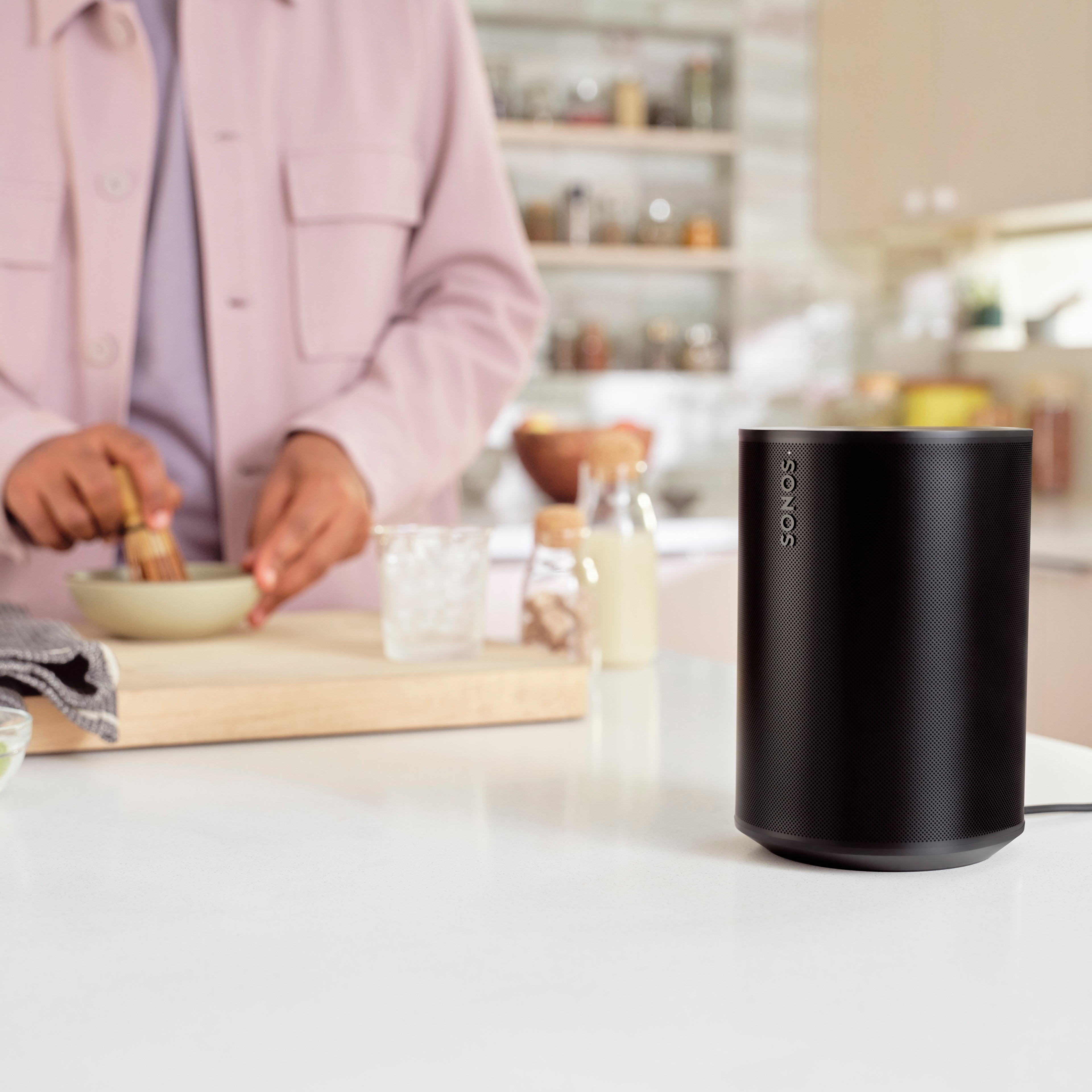 A black Era 100 speaker on a kitchen countertop next to someone preparing a drink