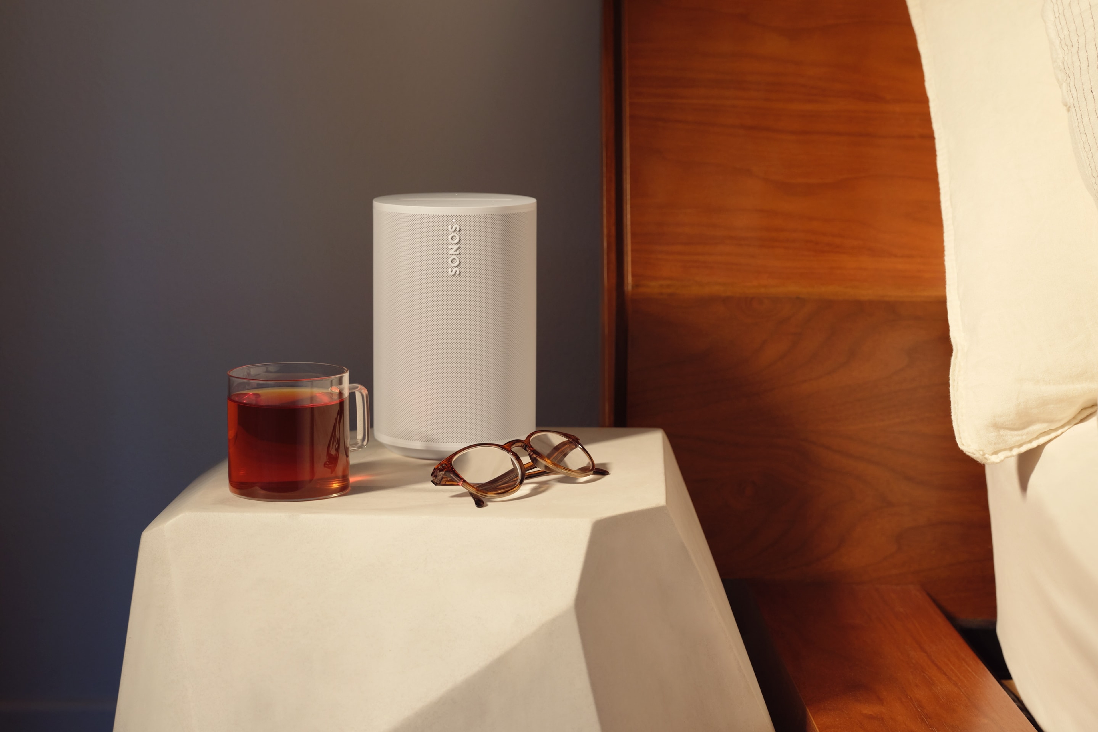 A white Era 100 speaker on a nightstand next to a bed
