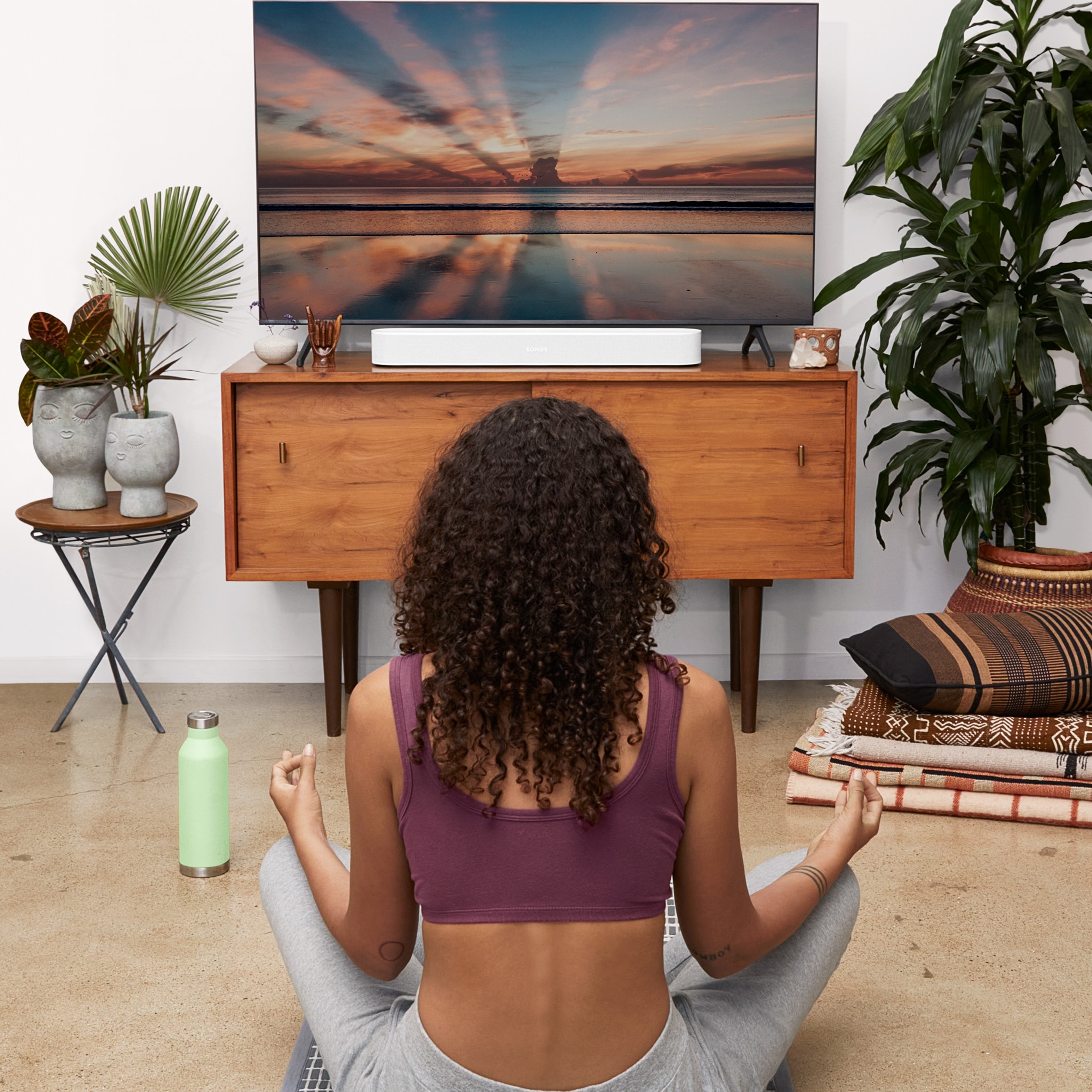 A woman sitting on the floor meditating in front of a TV with a white Sonos Beam soundbar