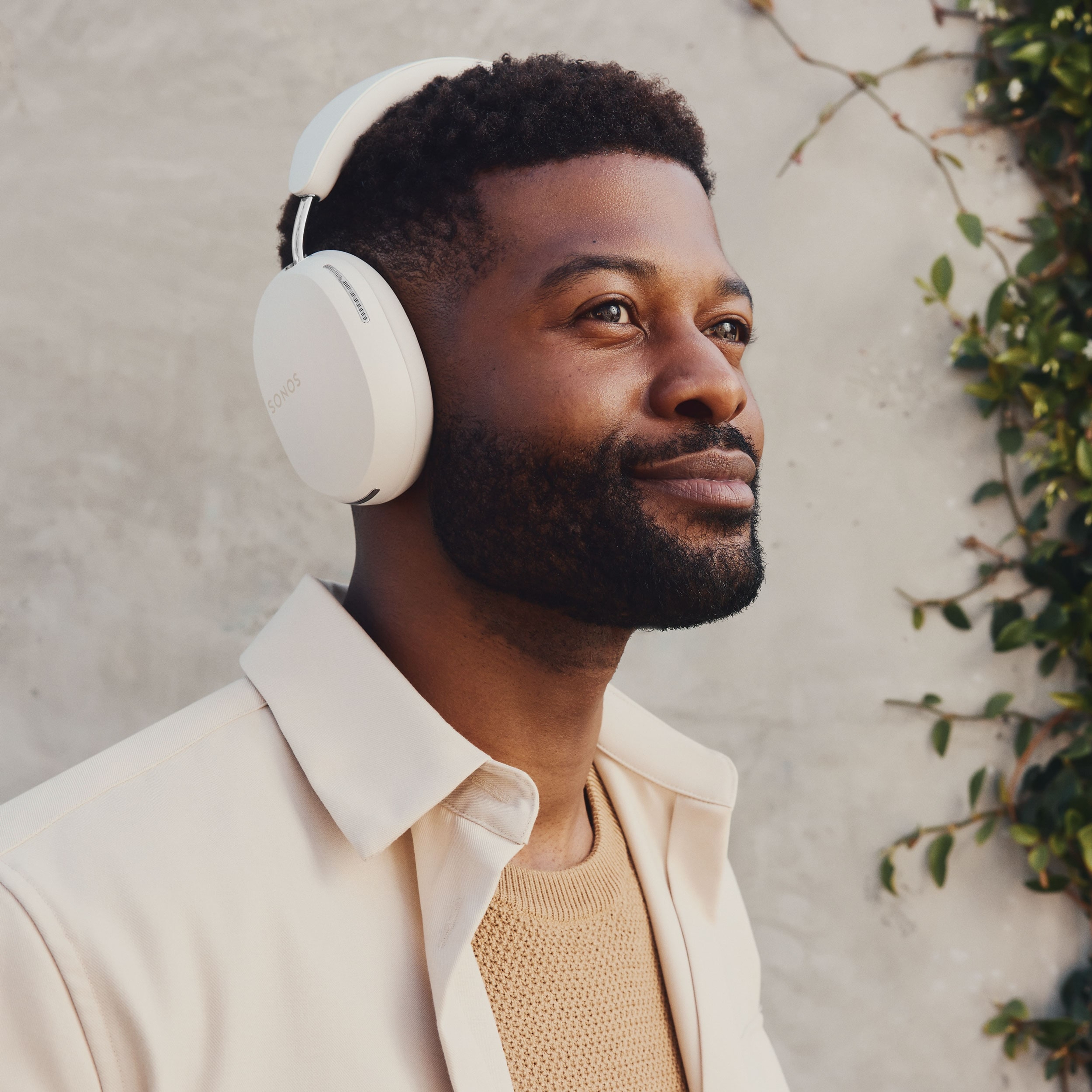 Une personne écoutant de la musique avec un casque Sonos Ace noir devant un mur en béton