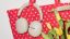 Une paire d’écouteurs Sonos Ace Ultra couleur Sand suspendus à un sac fourre-tout rouge à côté de fleurs