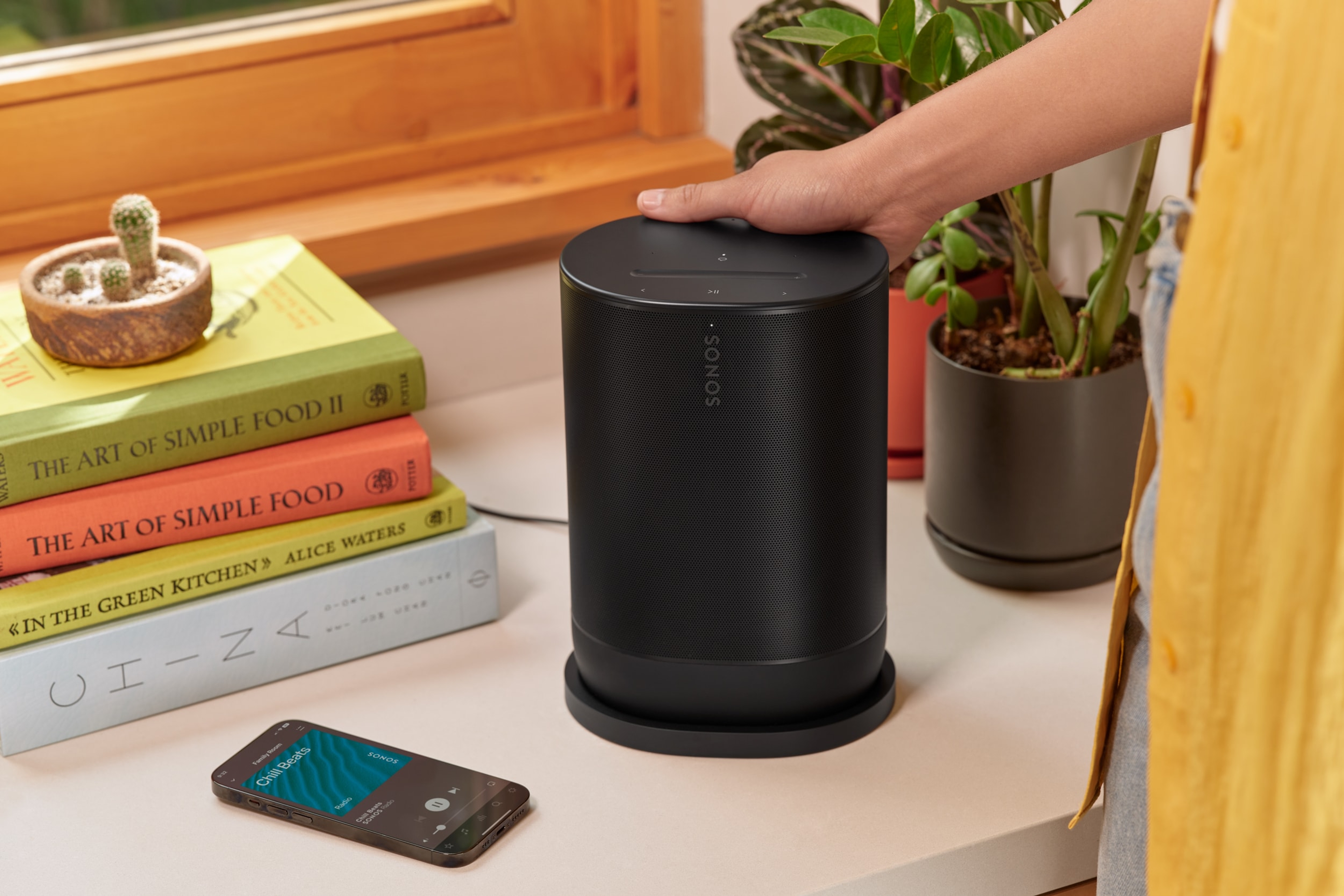 Image of a black Sonos Move 2 being placed on its charging base next to a stack of books and an iPhone