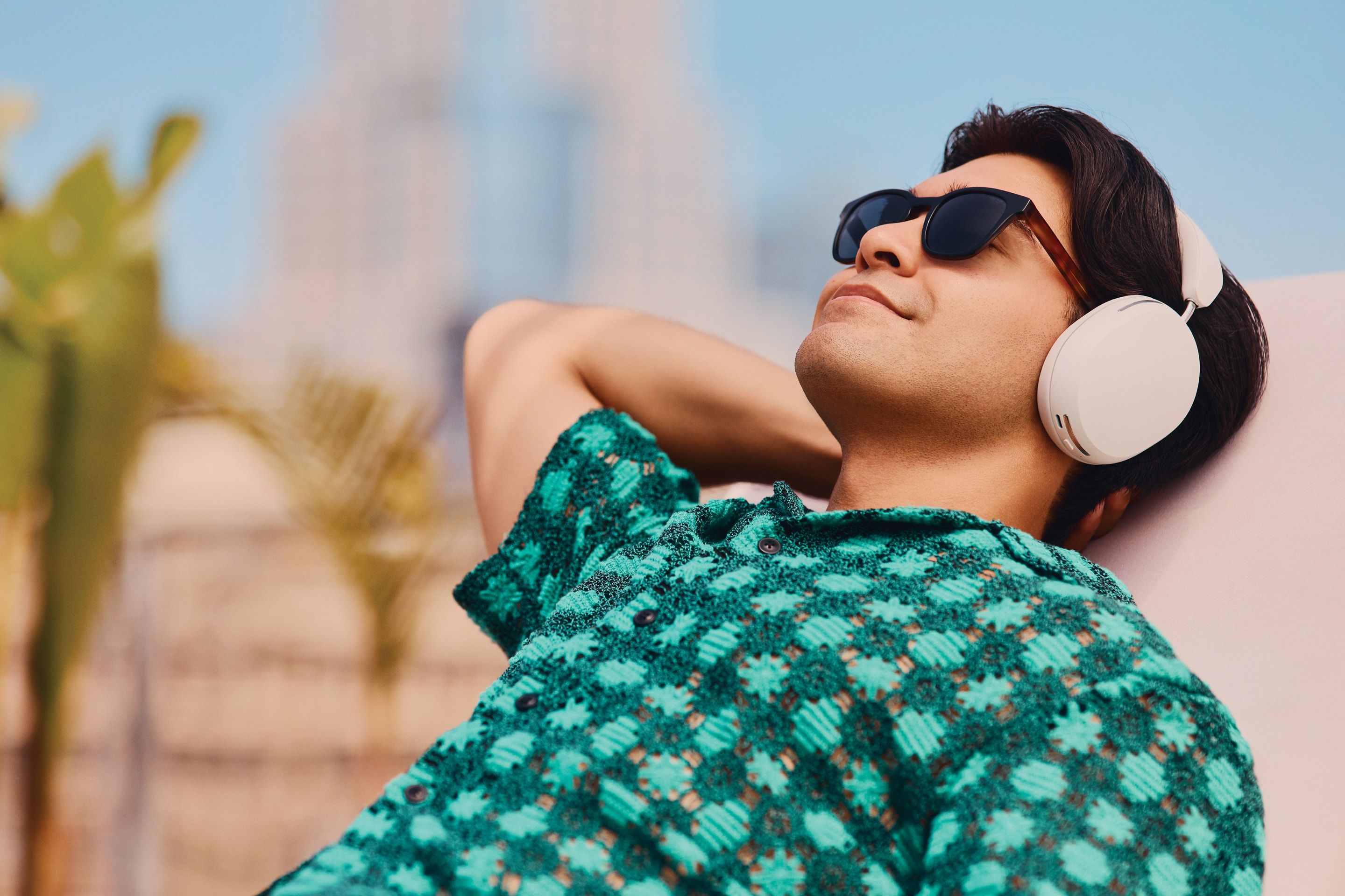 Person wearing a pair of Soft White Sonos Ace headphones while lounging on a chair outside