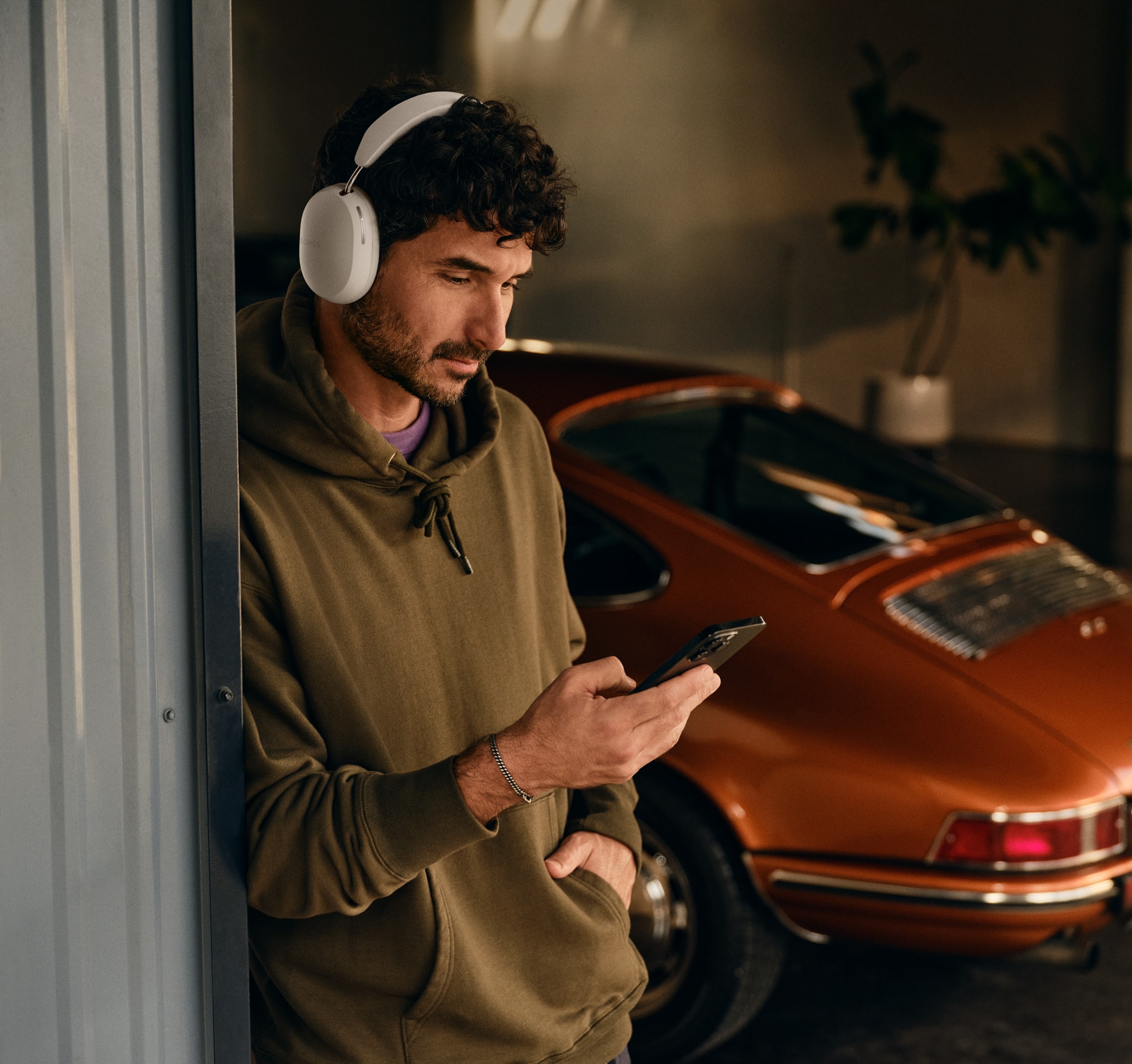 Osoba przy samochodzie, korzystająca z telefonu i z założonymi słuchawkami Sonos Ace w kolorze białym