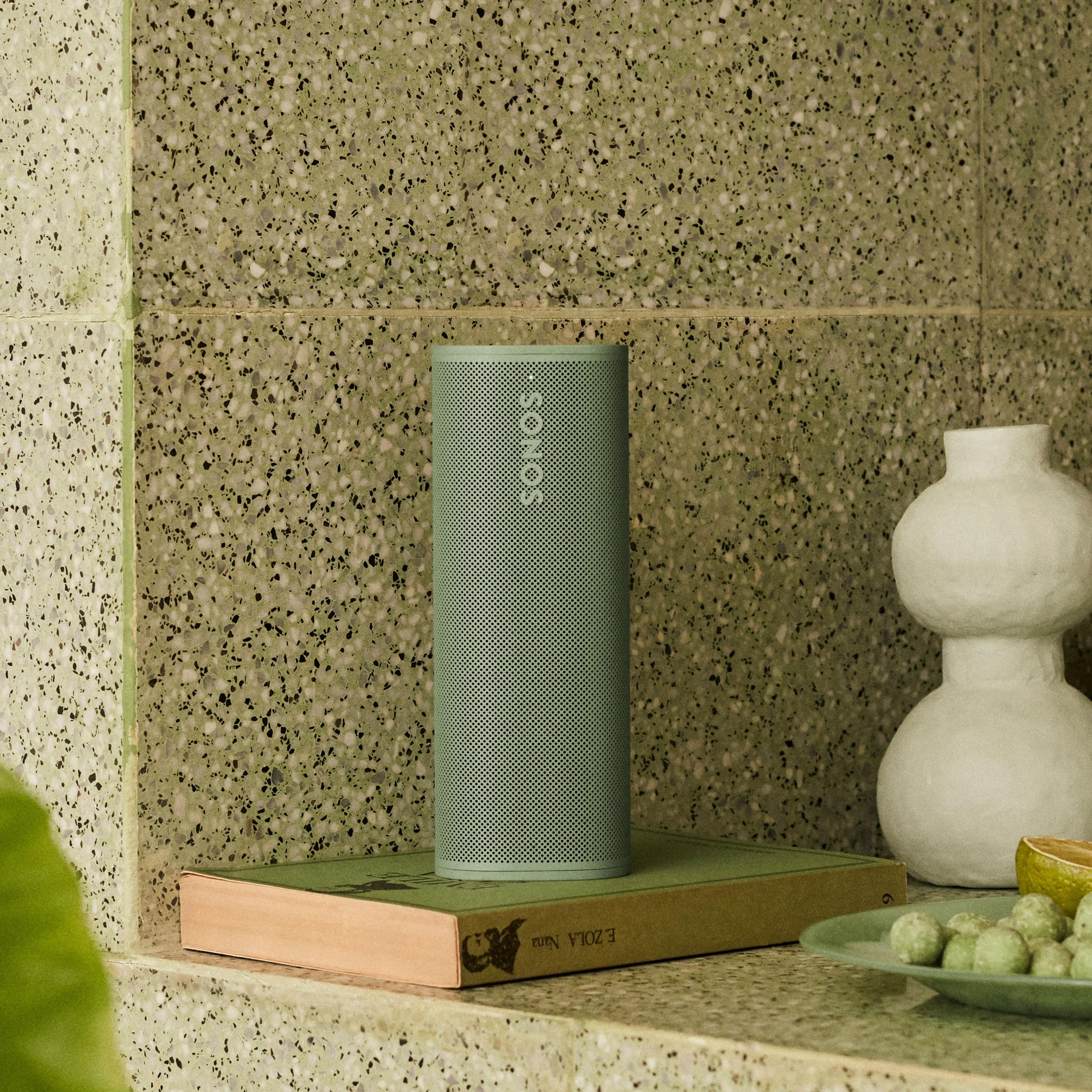 Sonos Roam 2 in Olive on top of a book and next to a vase