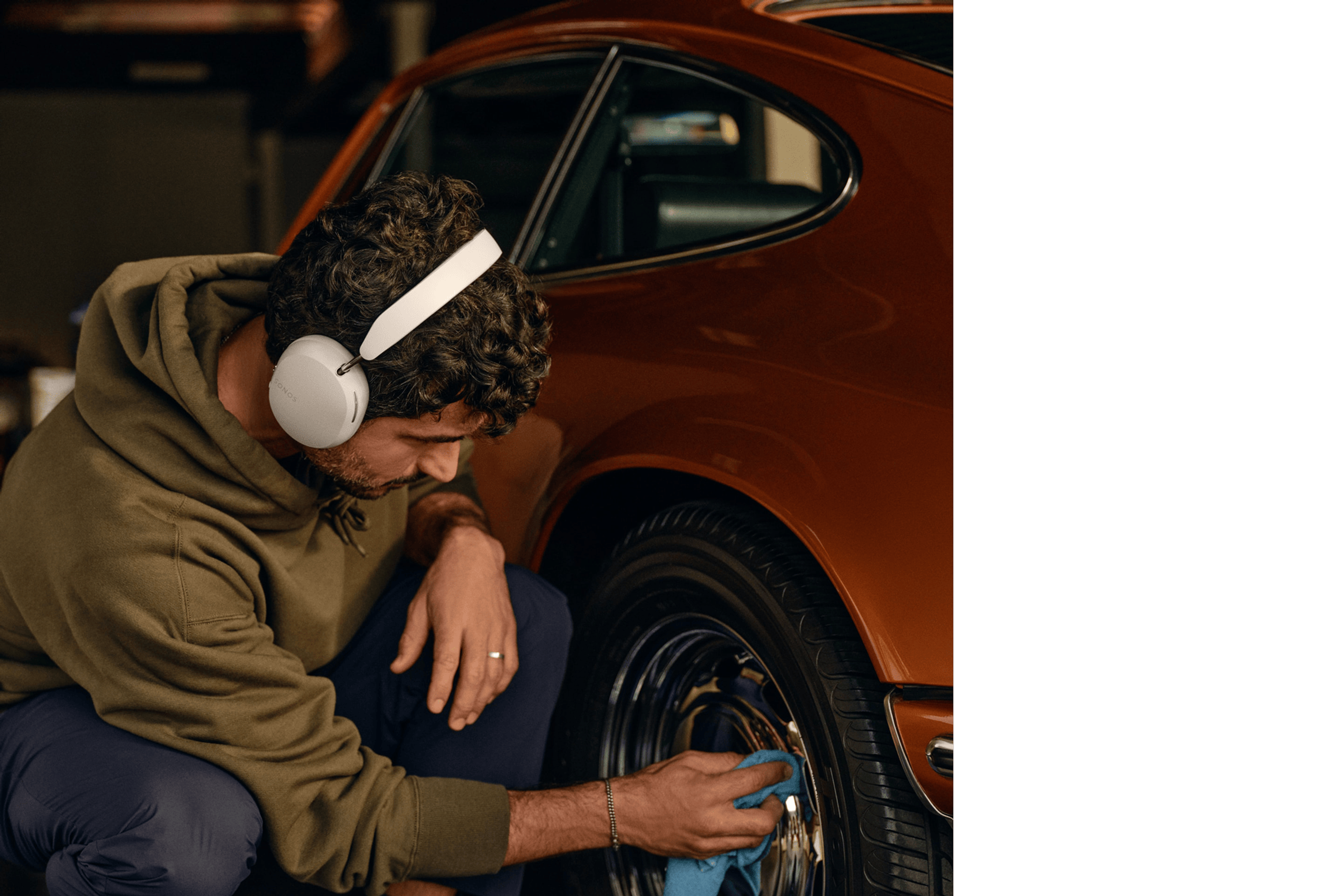 Un homme porte un casque audio Sonos Ace couleur Soft White tout en polissant les roues d'une voiture de collection