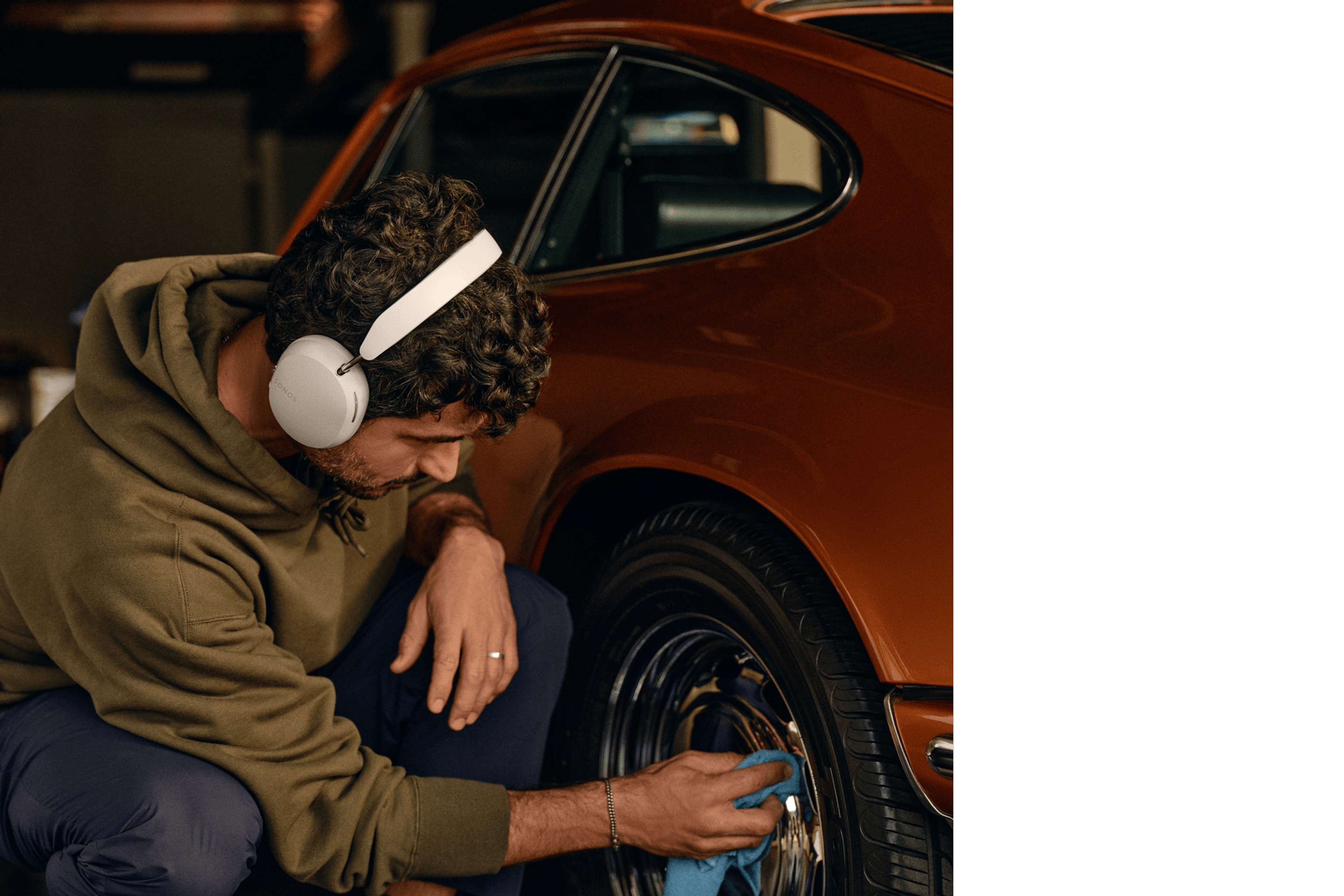 Una persona con unos auriculares Sonos Ace en blanco suave mientras pule las llantas de un coche clásico