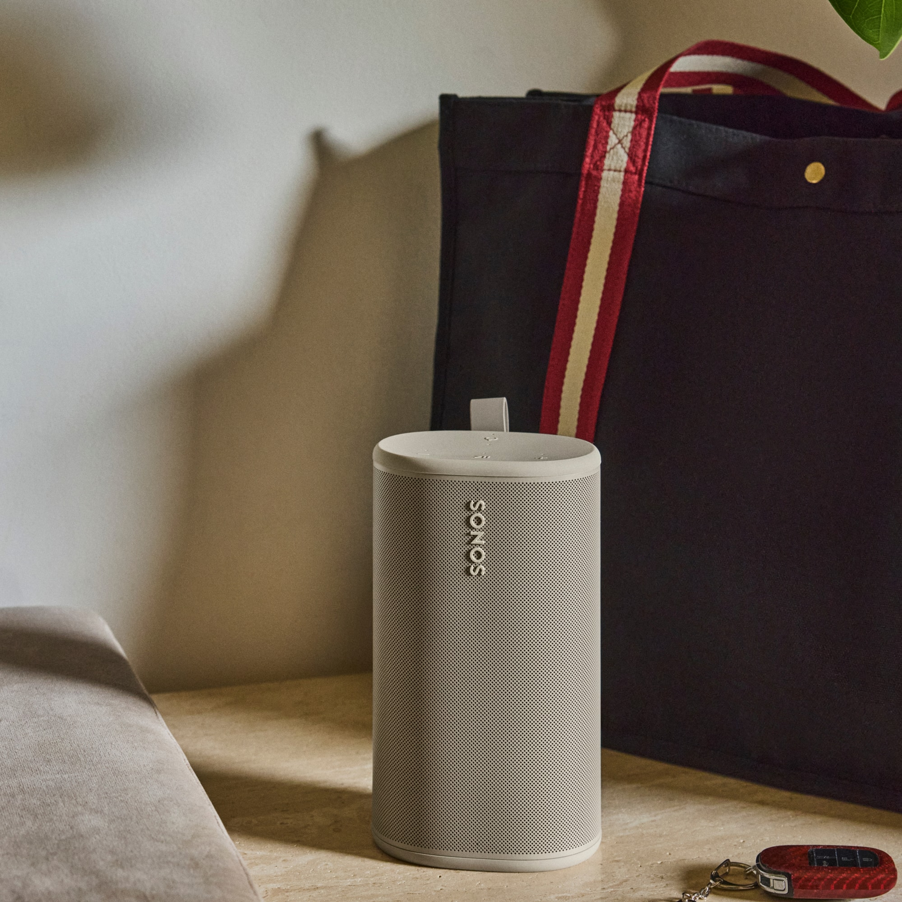 Une enceinte Sonos Play couleur Sable posée sur une surface en bois, à côté d’un sac cabas bleu marine et de clés