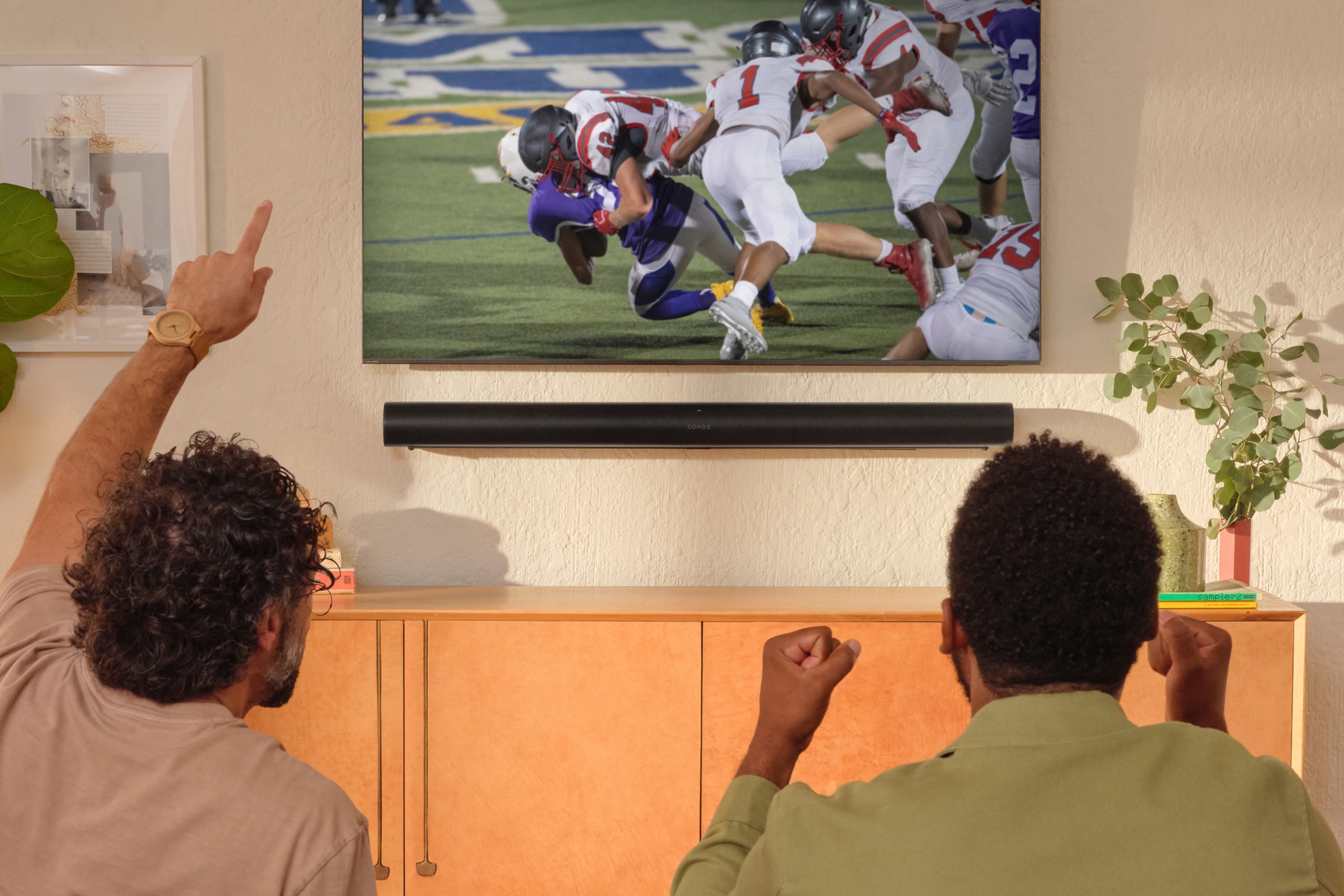 Friends on the couch watching a football game with a black Sonos Arc Ultra