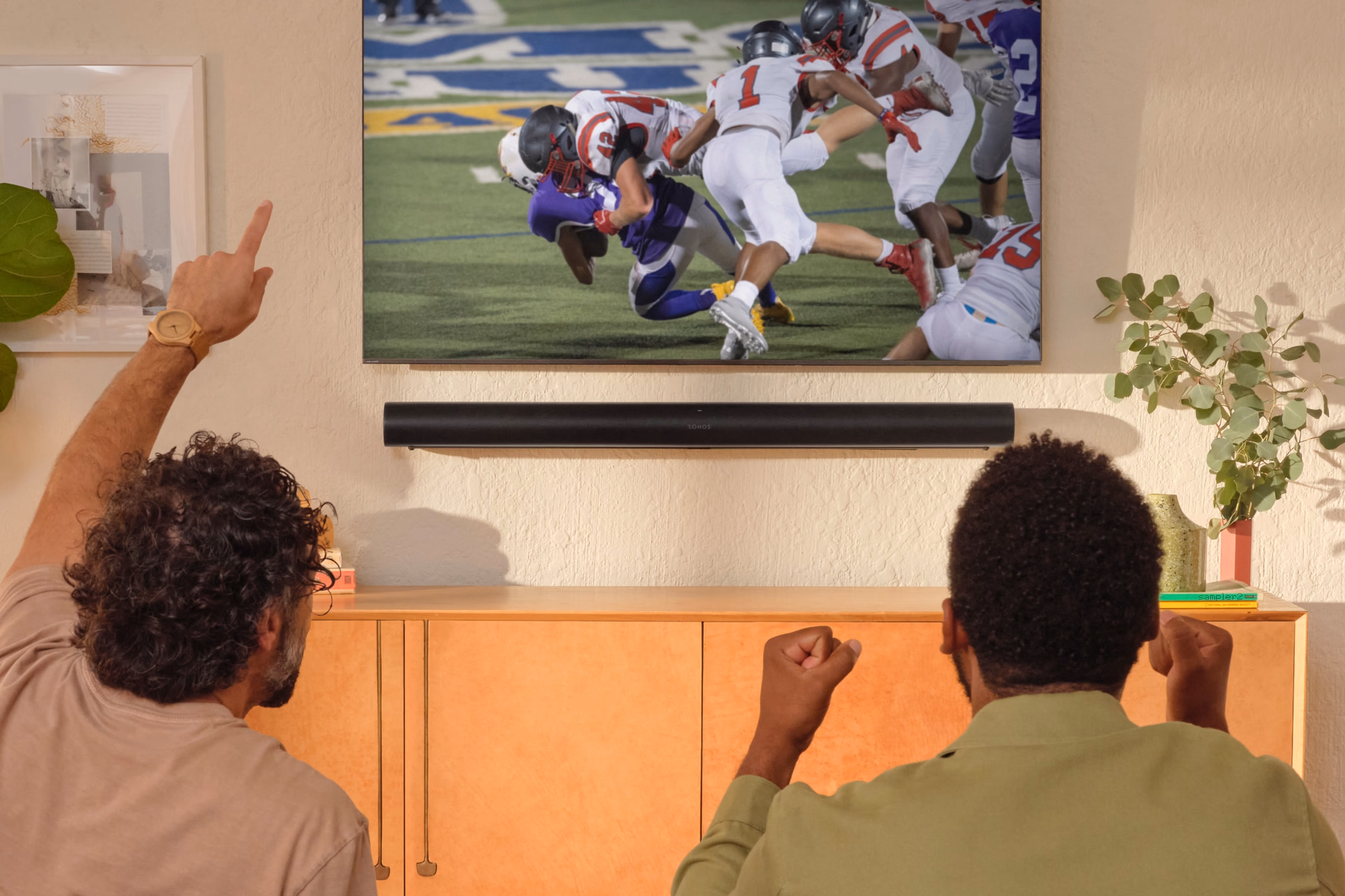 Friends on the couch watching a football game with a black Sonos Arc Ultra