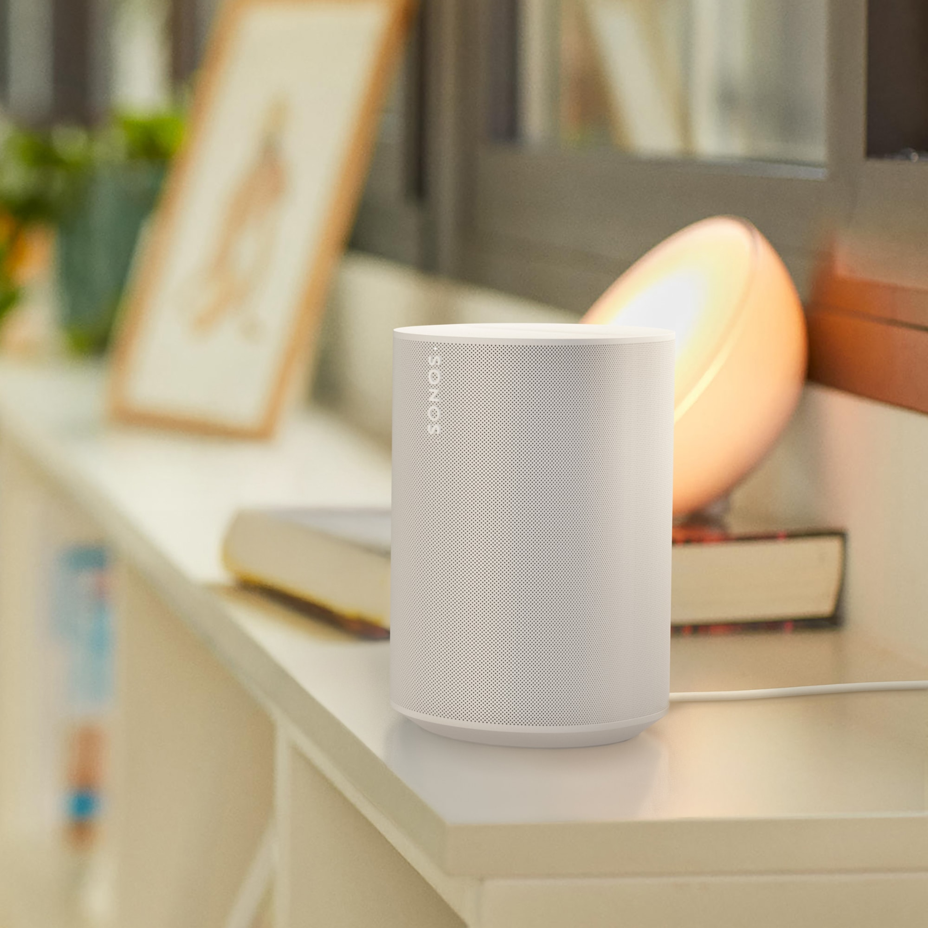 Une enceinte Sonos Era 100 blanche sur un buffet blanc à côté d'une lampe Philips Hue