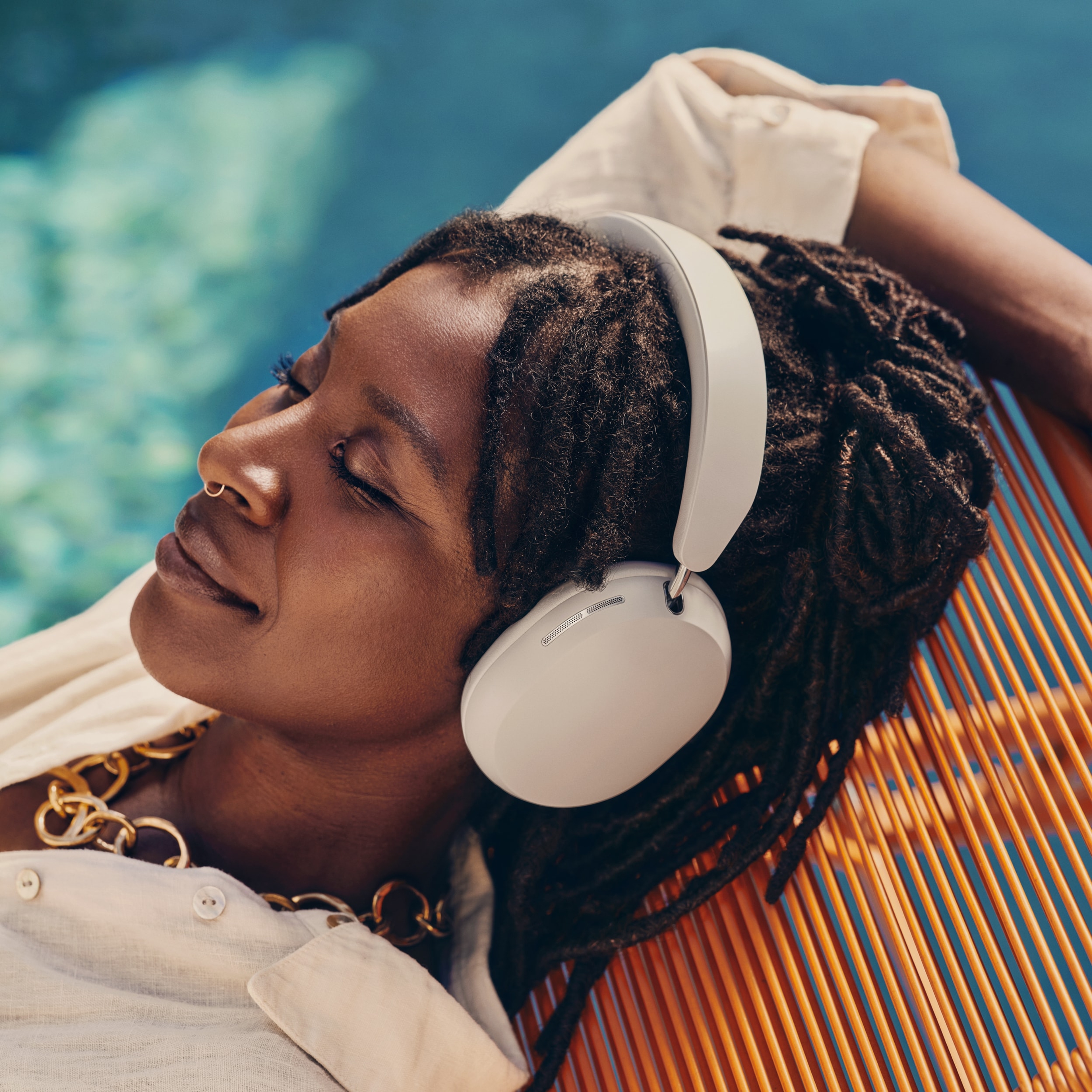 Une femme allongée au bord de la piscine porte un casque audio Sonos Ace couleur Soft White