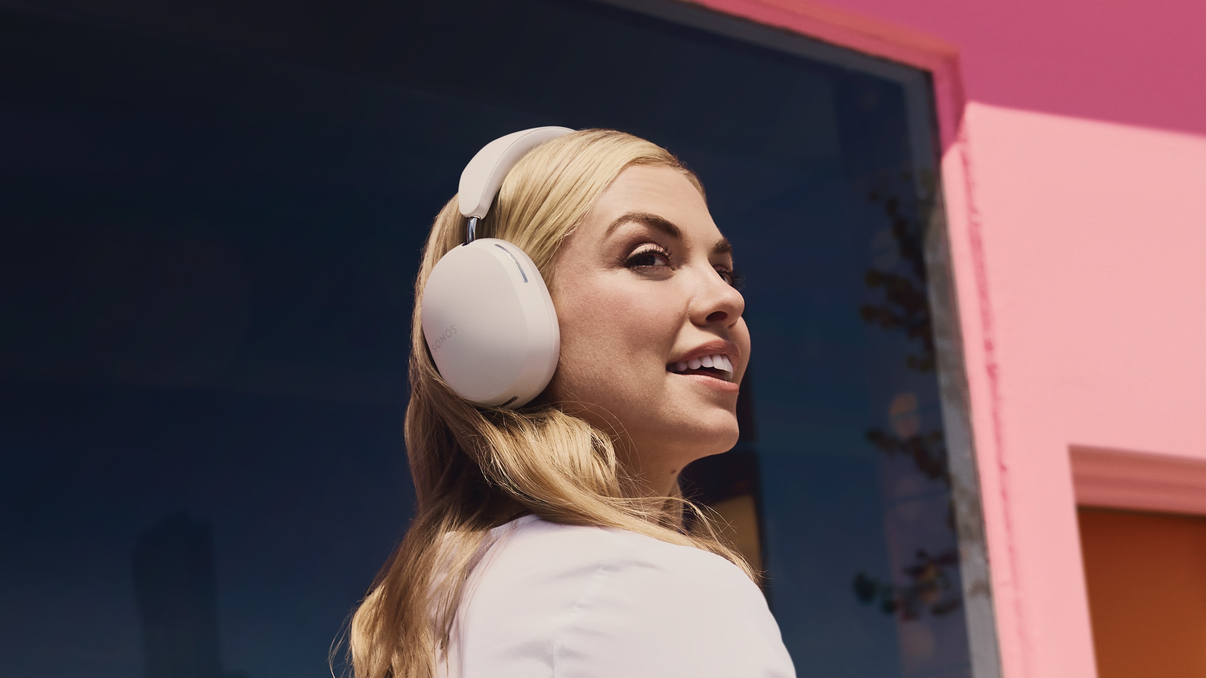 Person smiling wearing Sonos Ace in white next to a pink wall