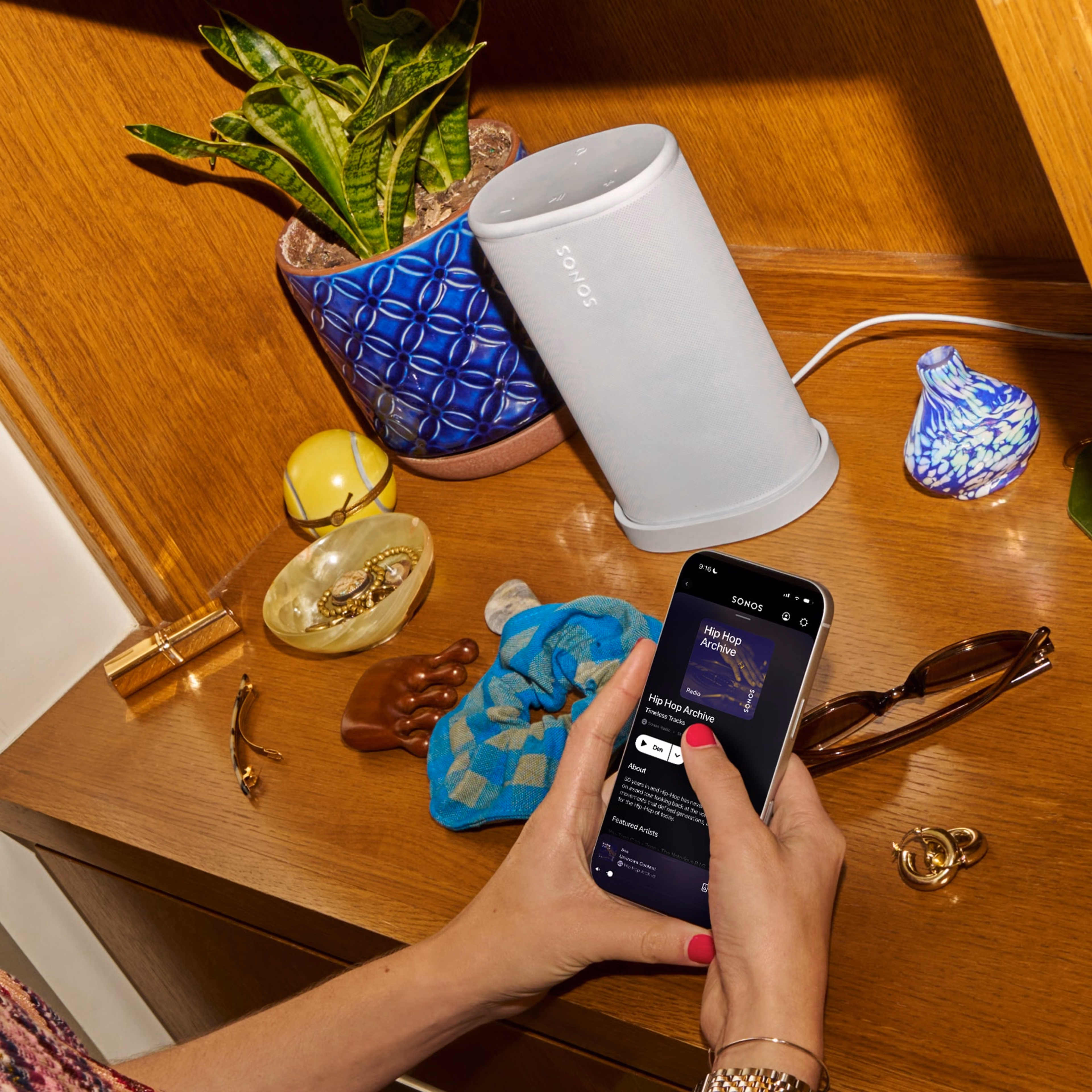 スマートフォンでSonosアプリを使用して、寝室のドレッサーに置かれたSonos Playスピーカー(ホワイト)を操作している人