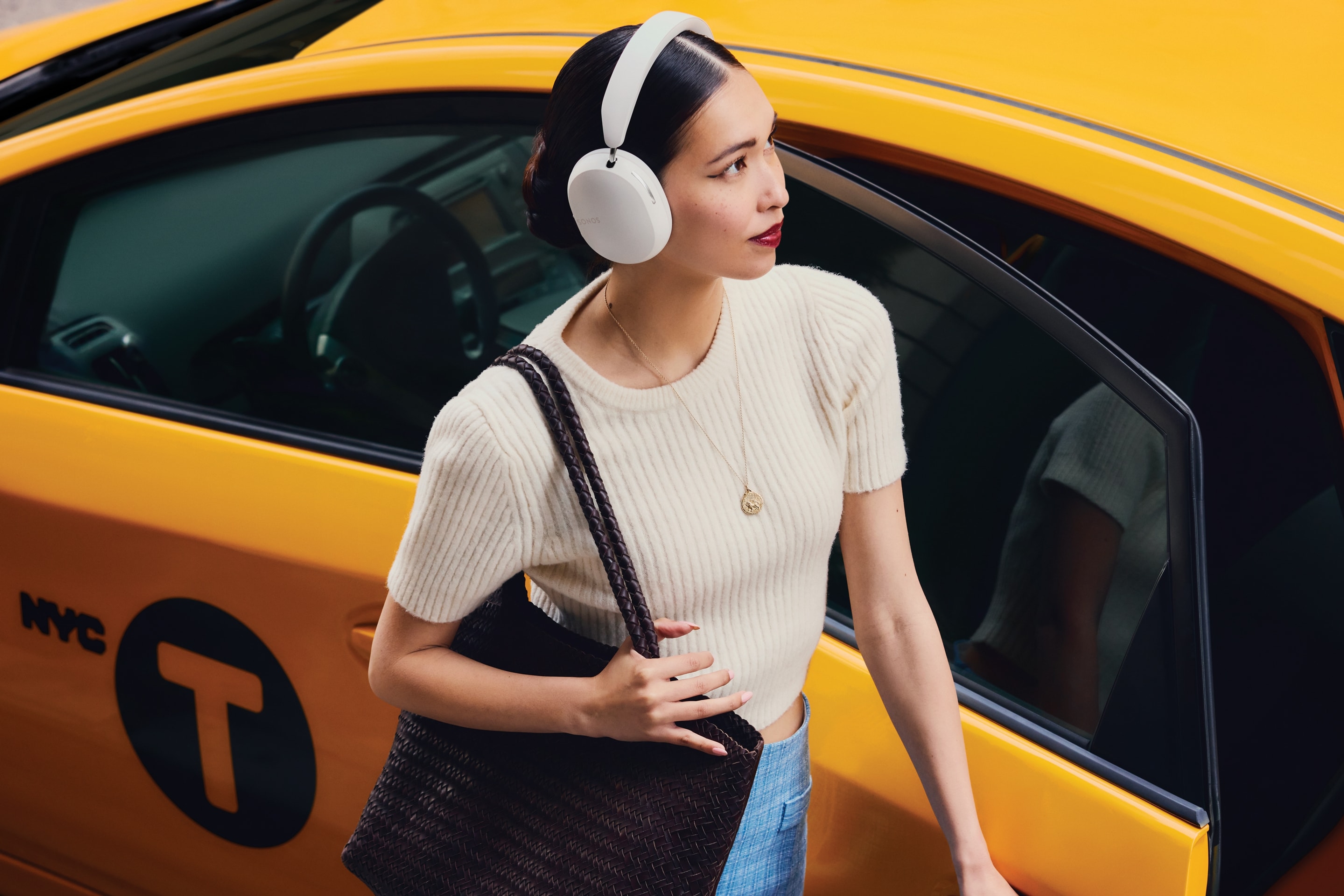 A commuter wearing soft white Sonos Ace headphones next to a taxi