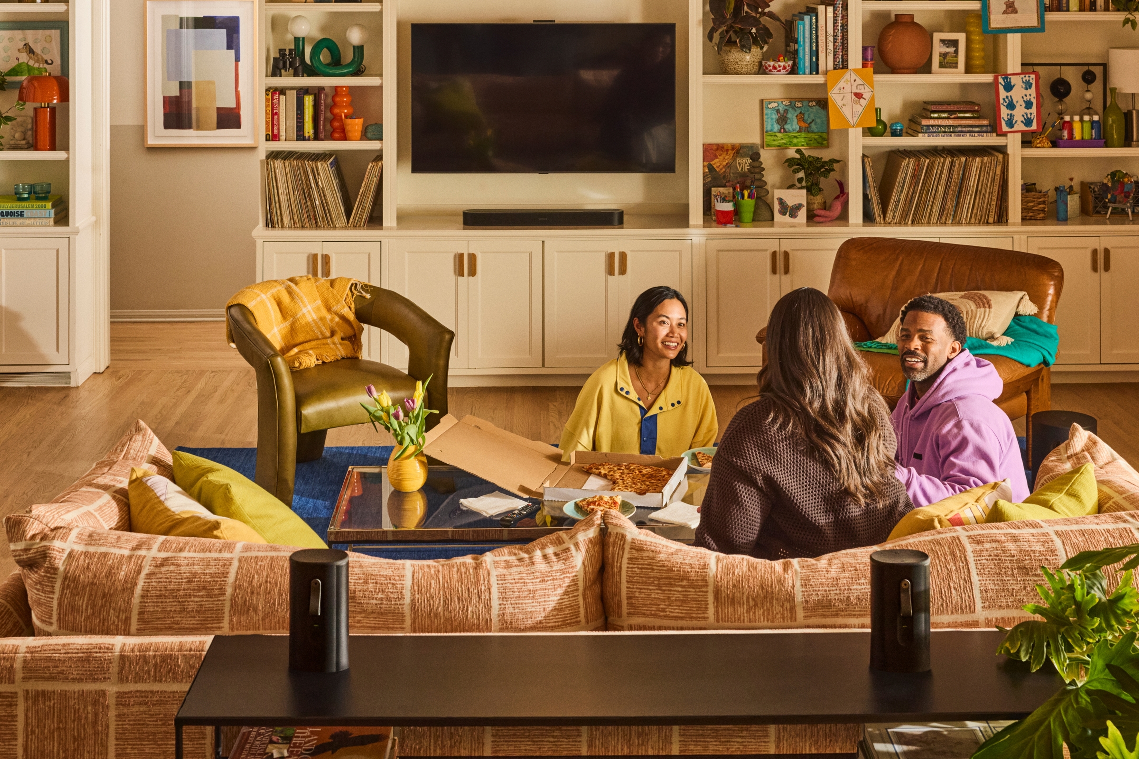 Three people gathered in a living room with a black Sonos Beam Ultra soundbar and a pair of Sonos Play