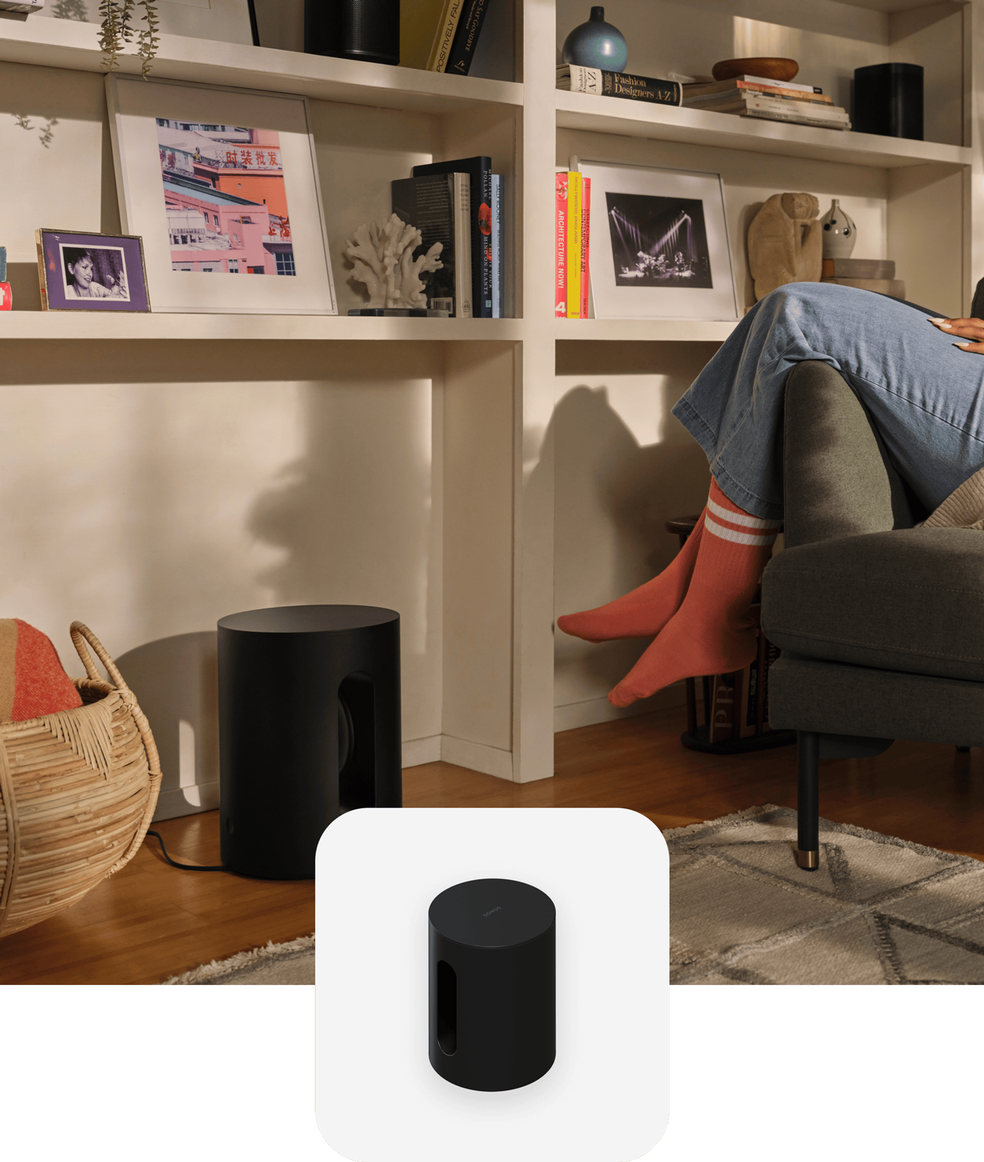 User sitting in living room armchair next to a black Sonos Sub Mini