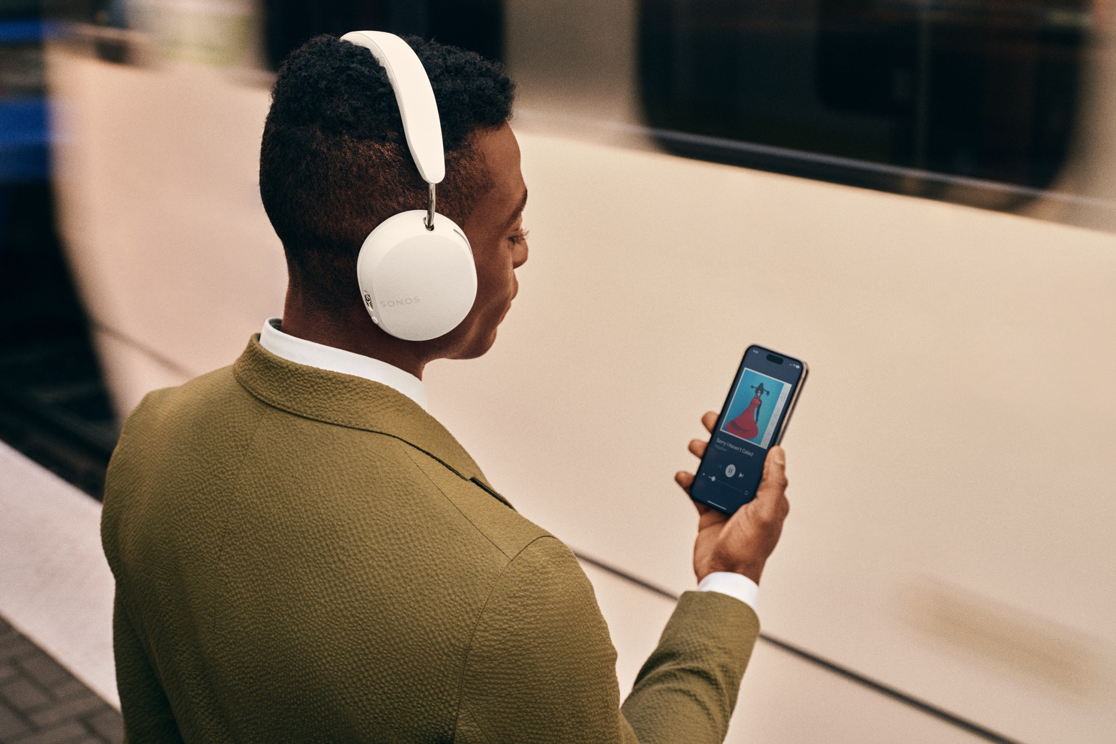Forens die een witte Sonos Ace koptelefoon gebruikt op een treinstation