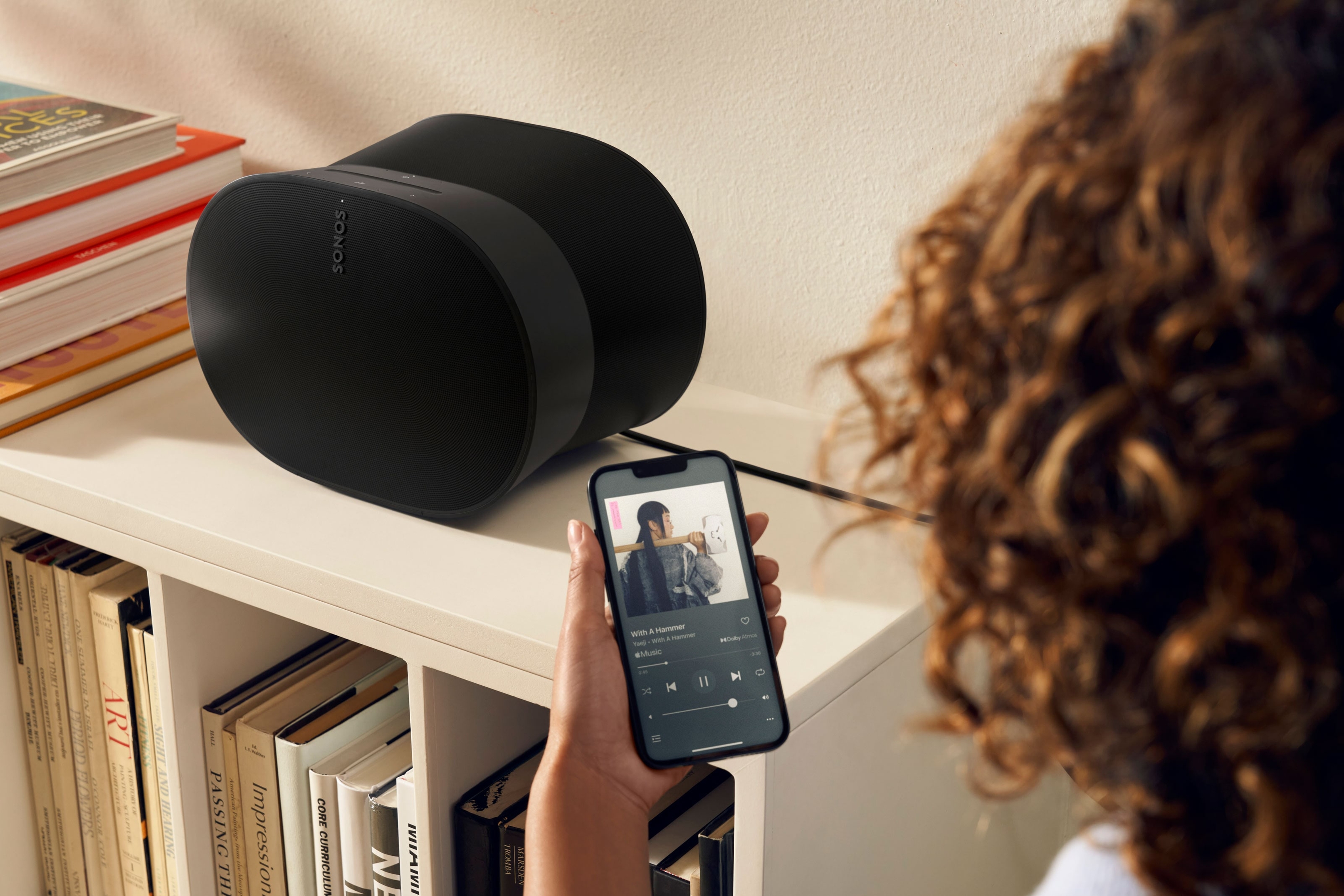Woman using her phone to control a black Era 300 on a bookshelf