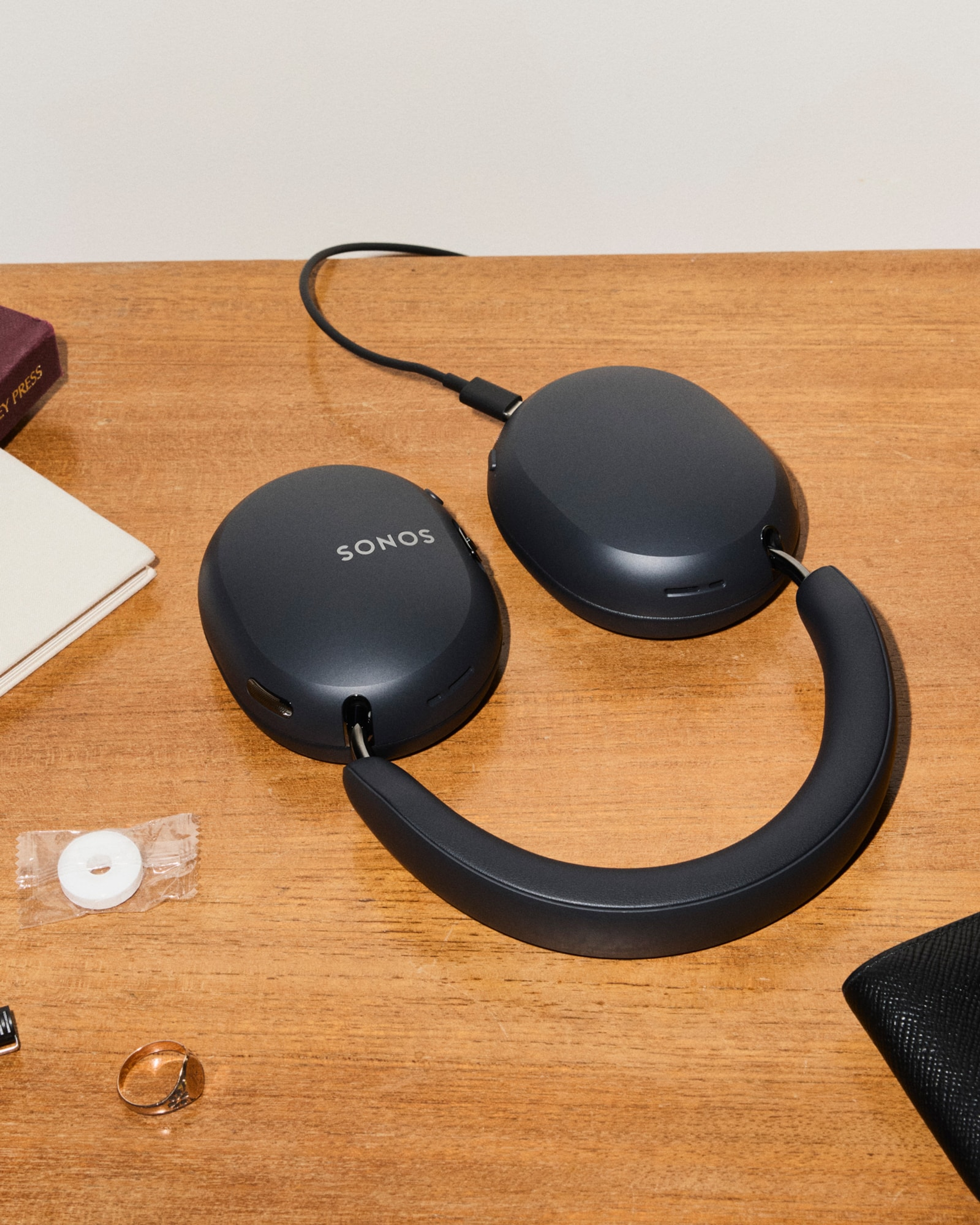 A pair of black Sonos Ace Ultra headphones laying flat on a table plugged into USB-C to recharge