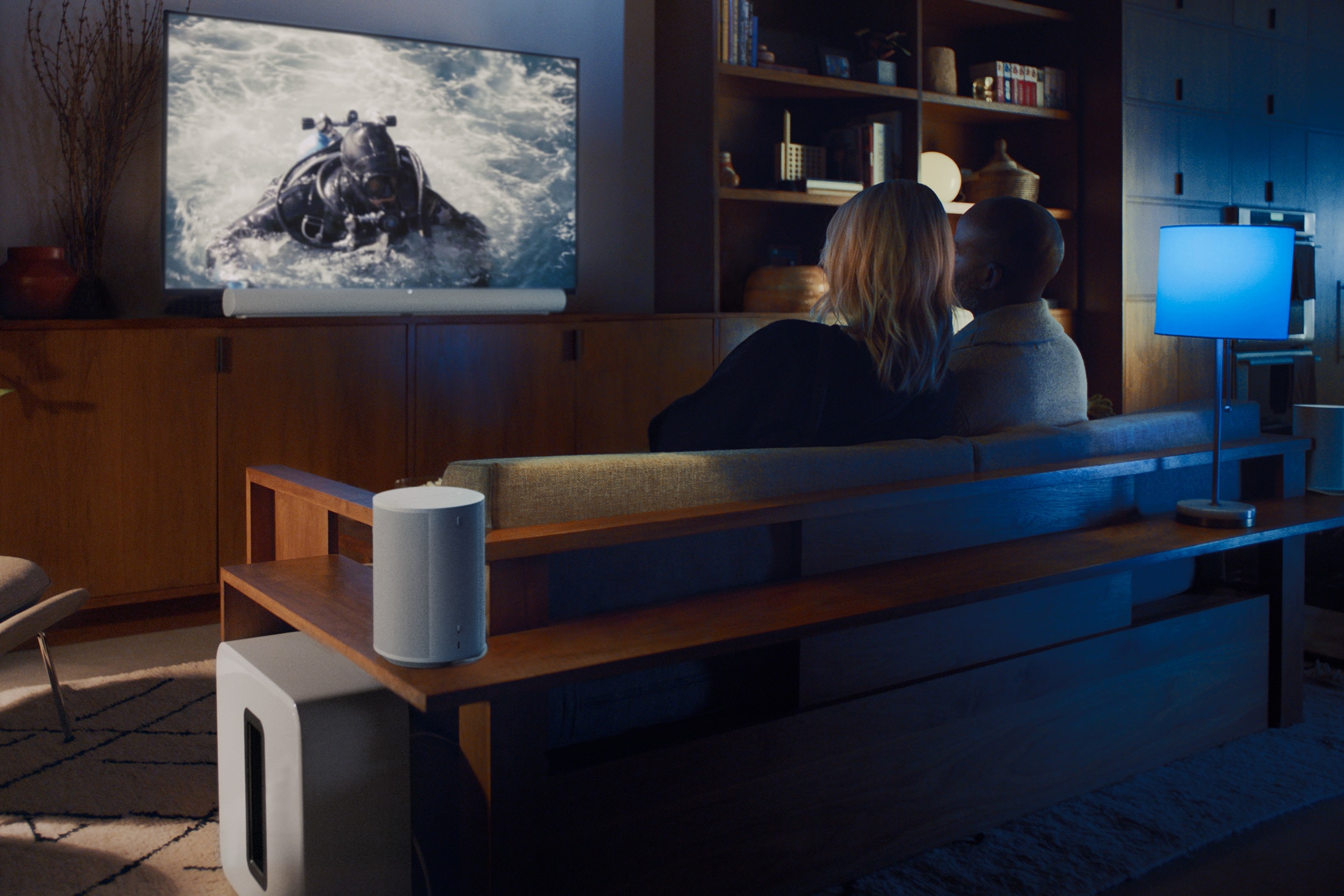 Un couple assis sur un canapé en train de regarder un film avec un système home cinéma Sonos comprenant une Sonos Arc Ultra, un Sonos Sub 4 et des Sonos Era 100