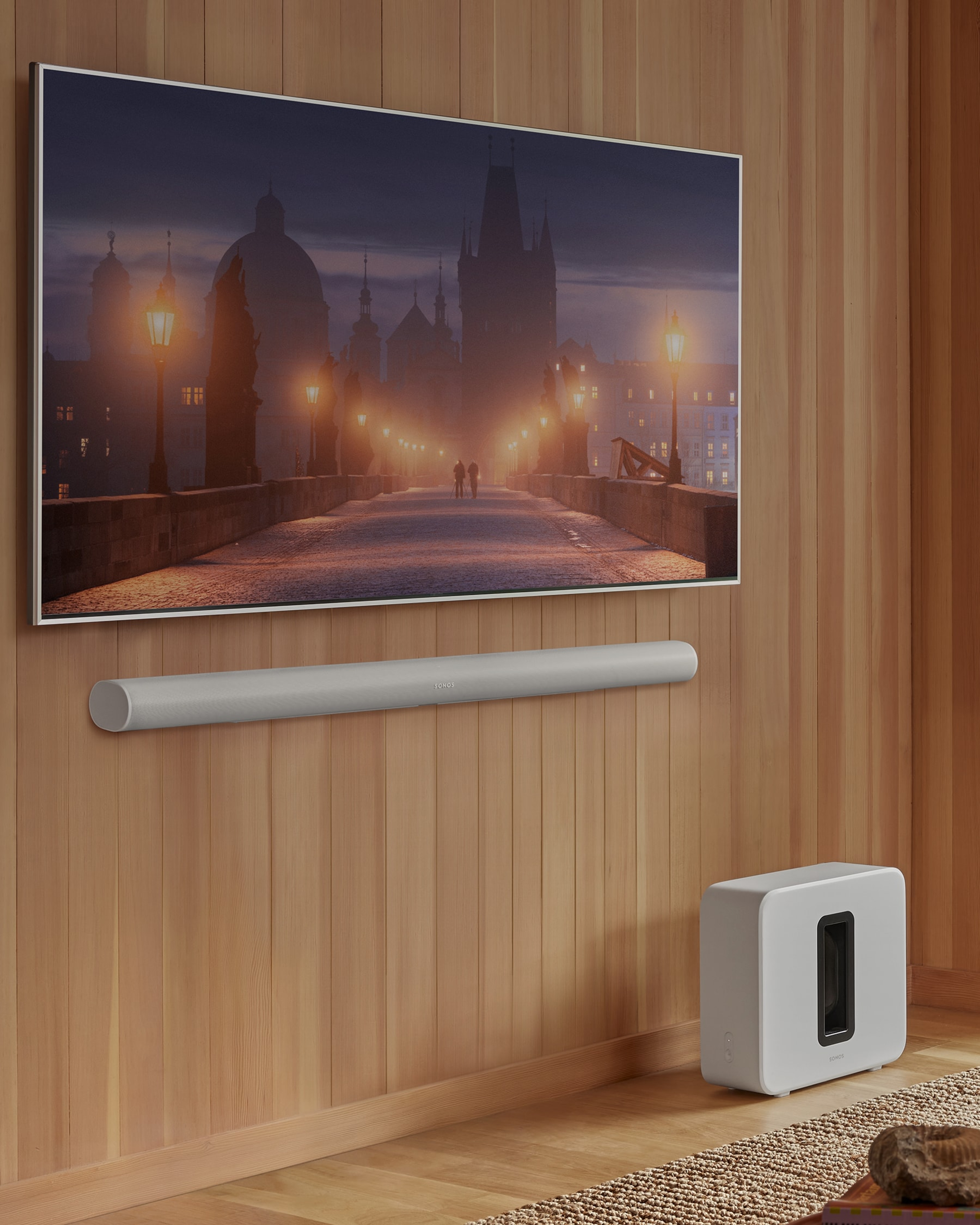 Une Sonos Arc Ultra fixée au mur et un Sonos Sub 4 placé au sol, en blanc