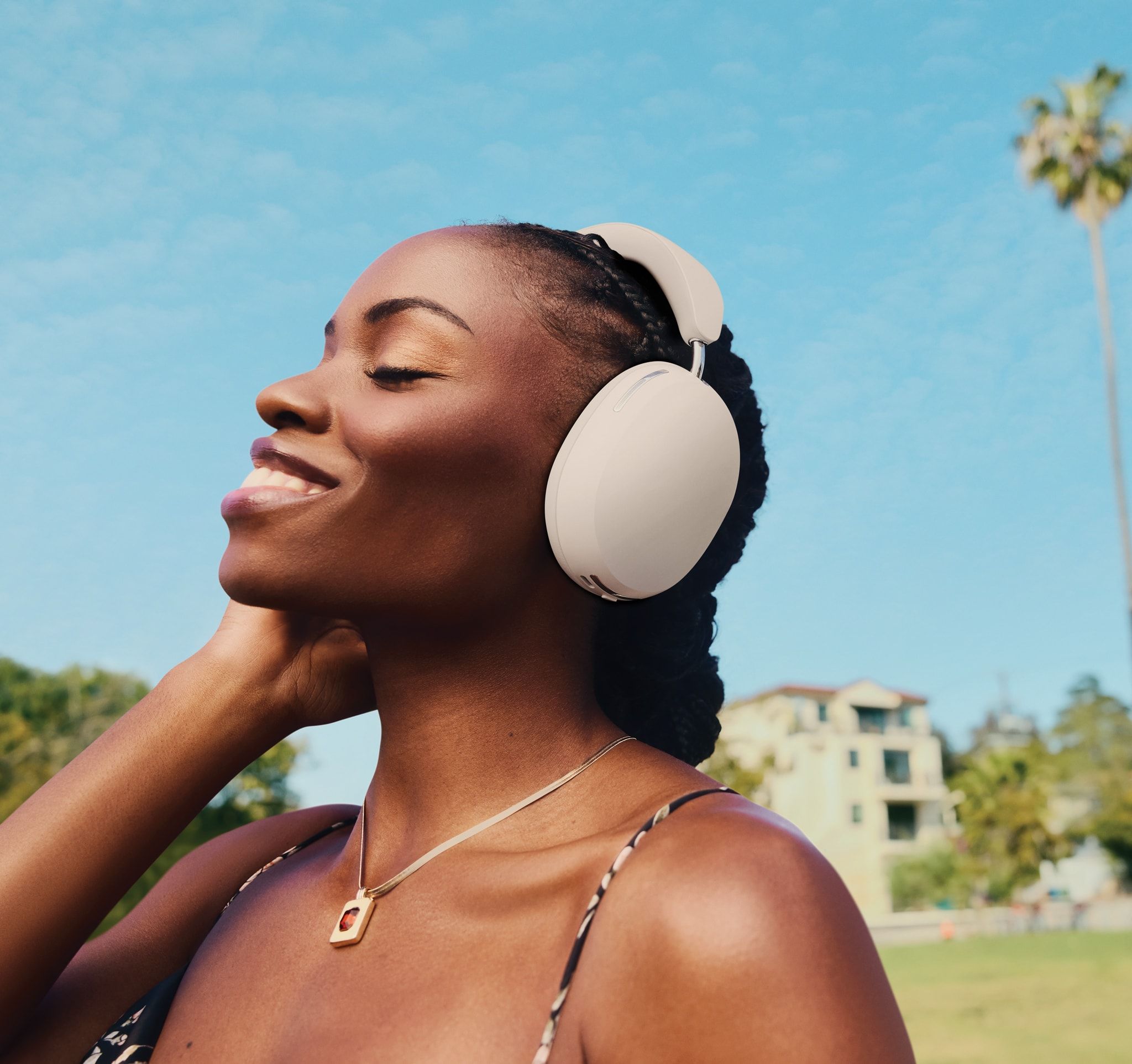 Person smiling and listening to music on Soft White Sonos Ace headphones outside