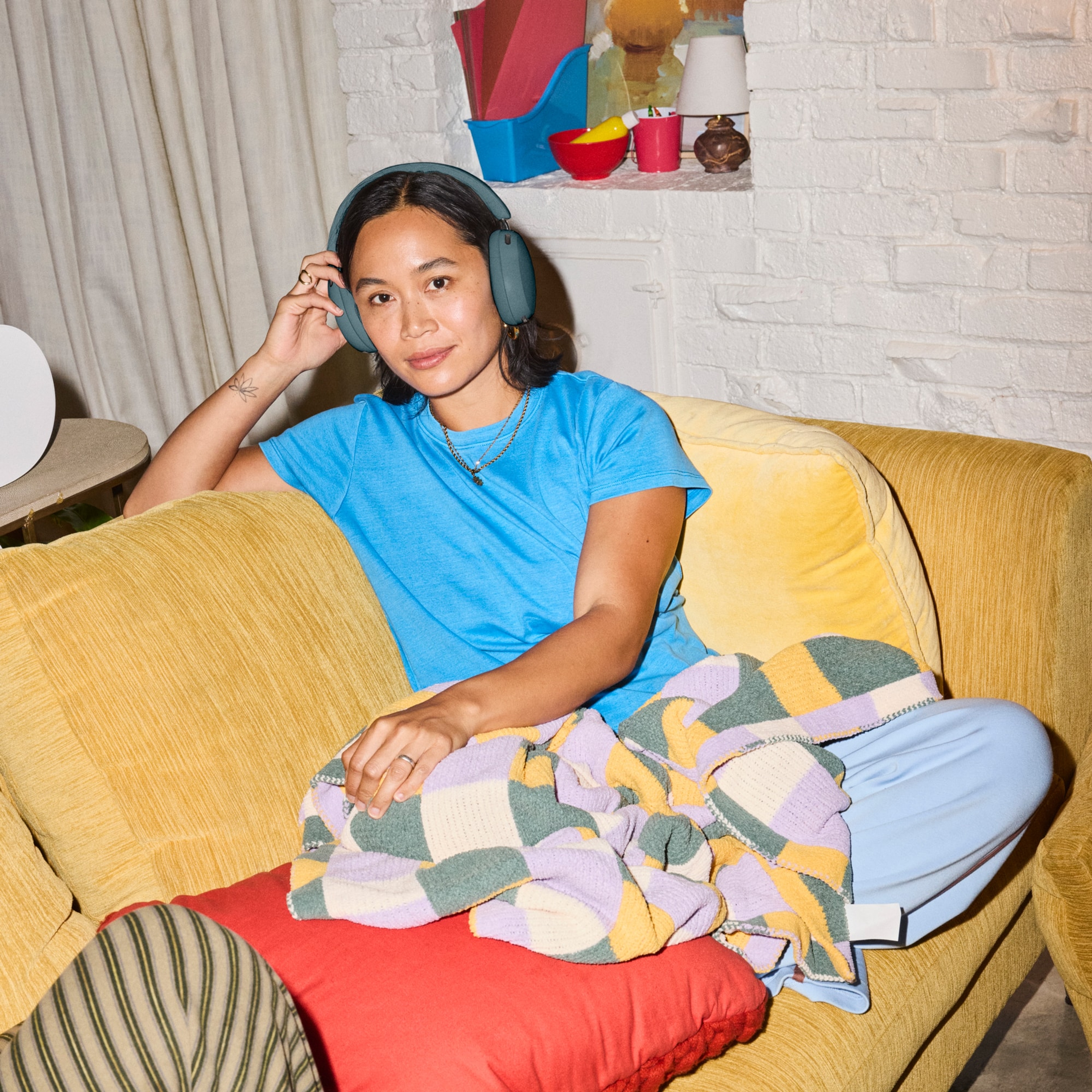 Person wearing Sonos Ace Ultra headphones in Agave sitting on a yellow couch in a living room