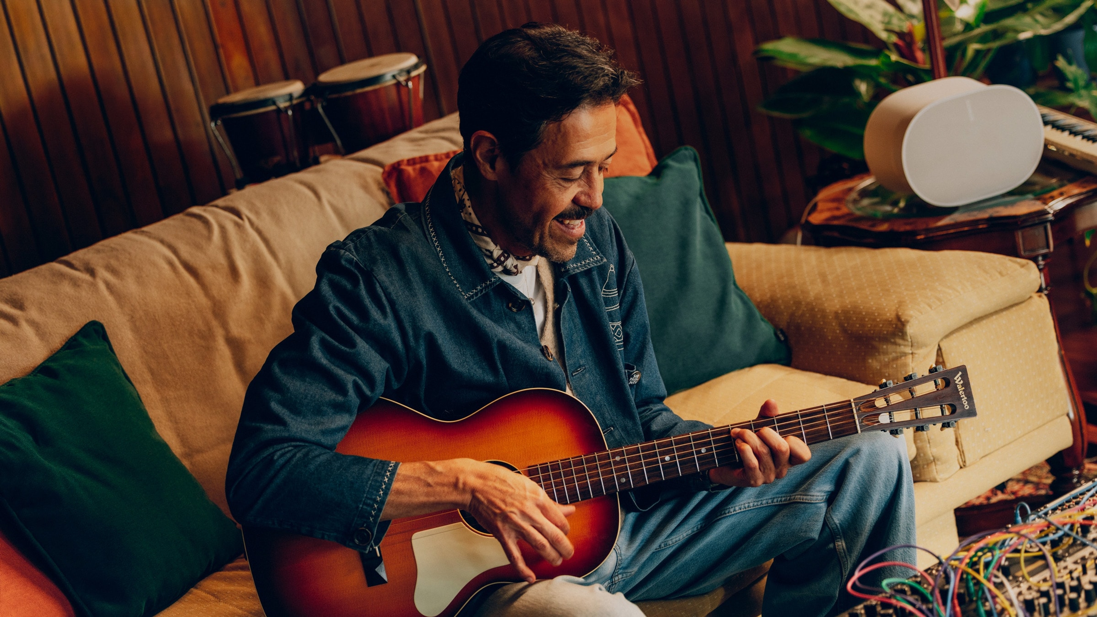 El músico Emmanuel del Real tocando la guitarra junto a un altavoz Sonos Era 300 blanco