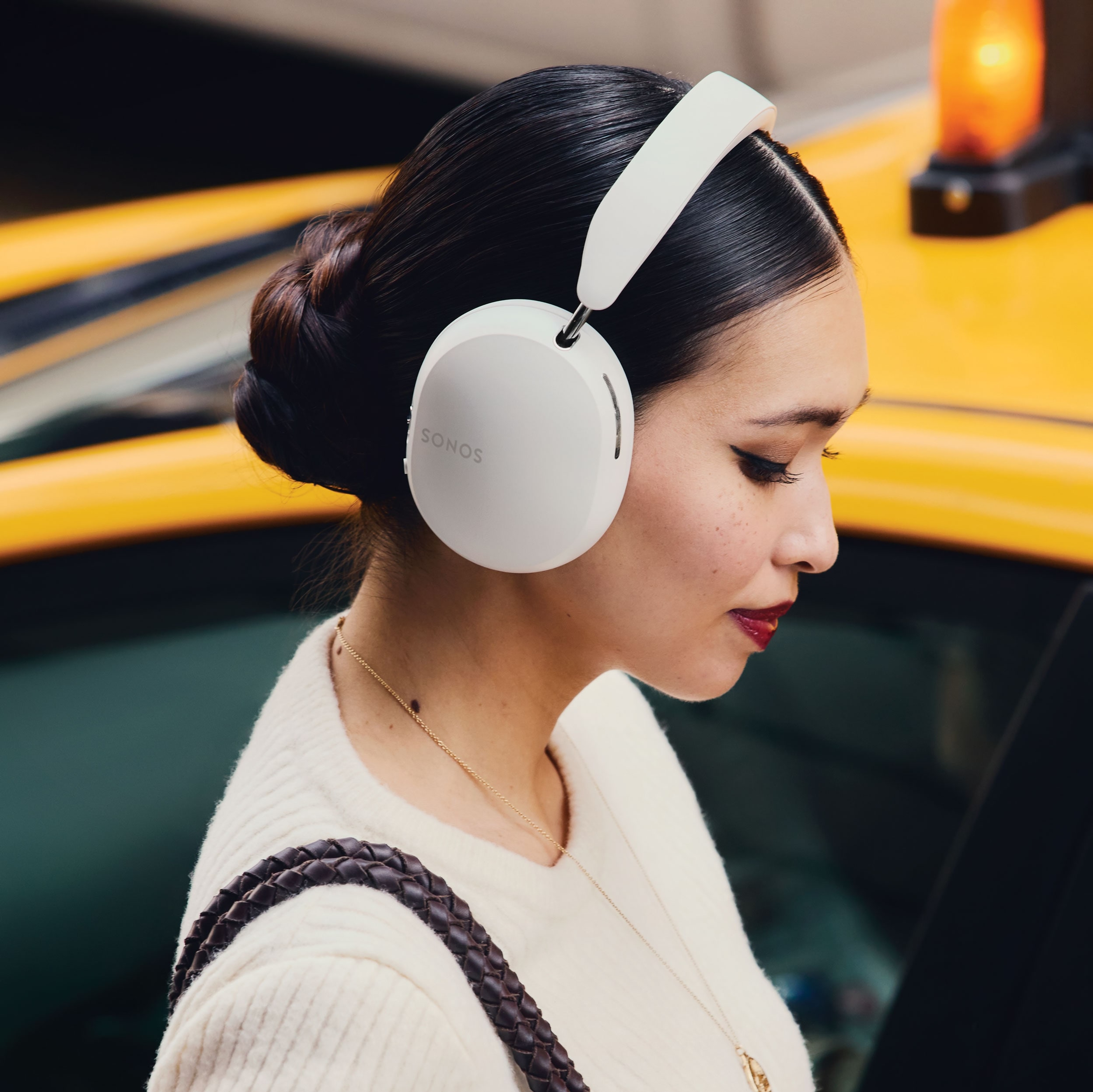 A commuter wearing soft white Sonos Ace headphones next to a taxi