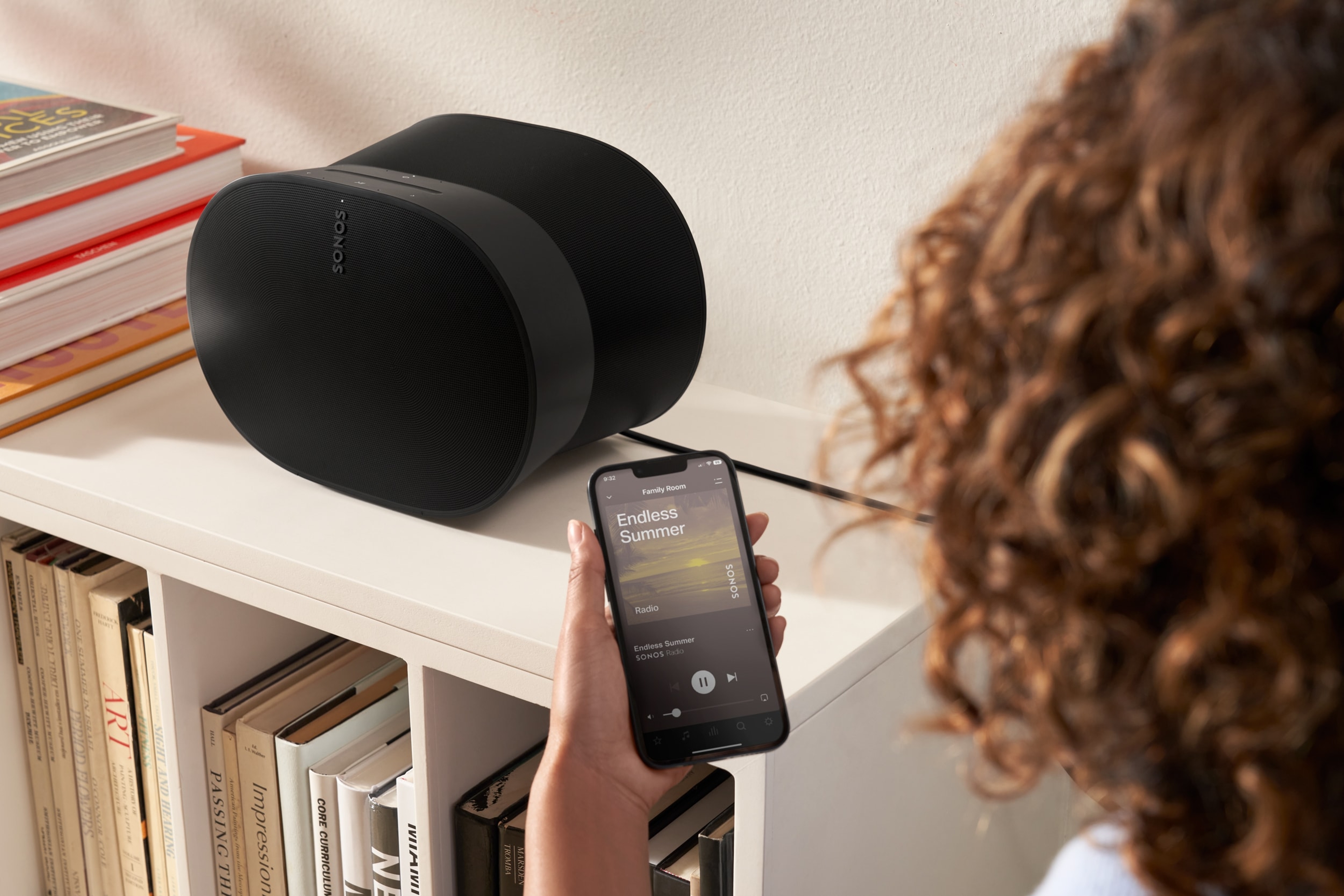 Woman using her phone to control a black Era 300 on a bookshelf