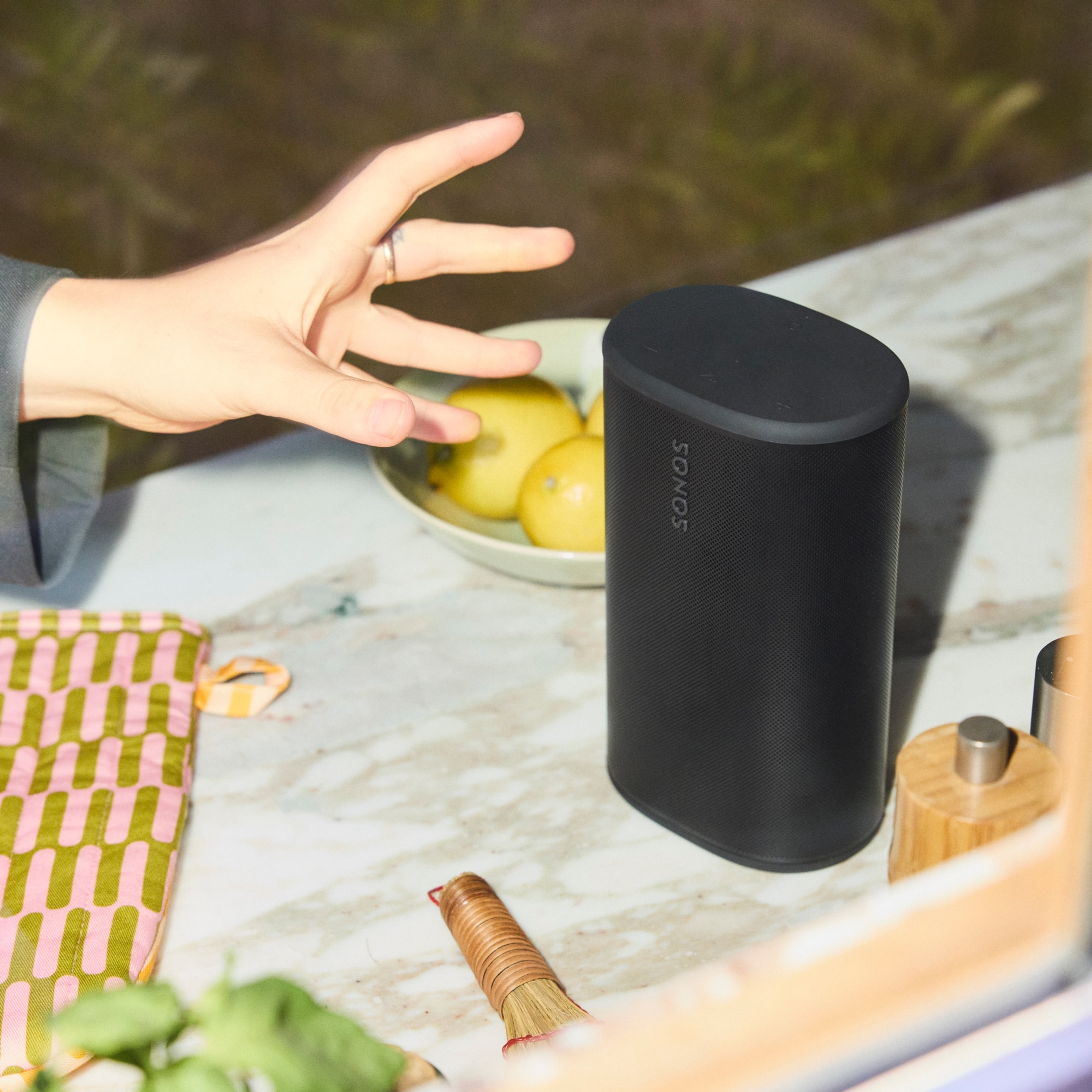 Person reaching across the kitchen counter to pick up a black Sonos Play portable speaker