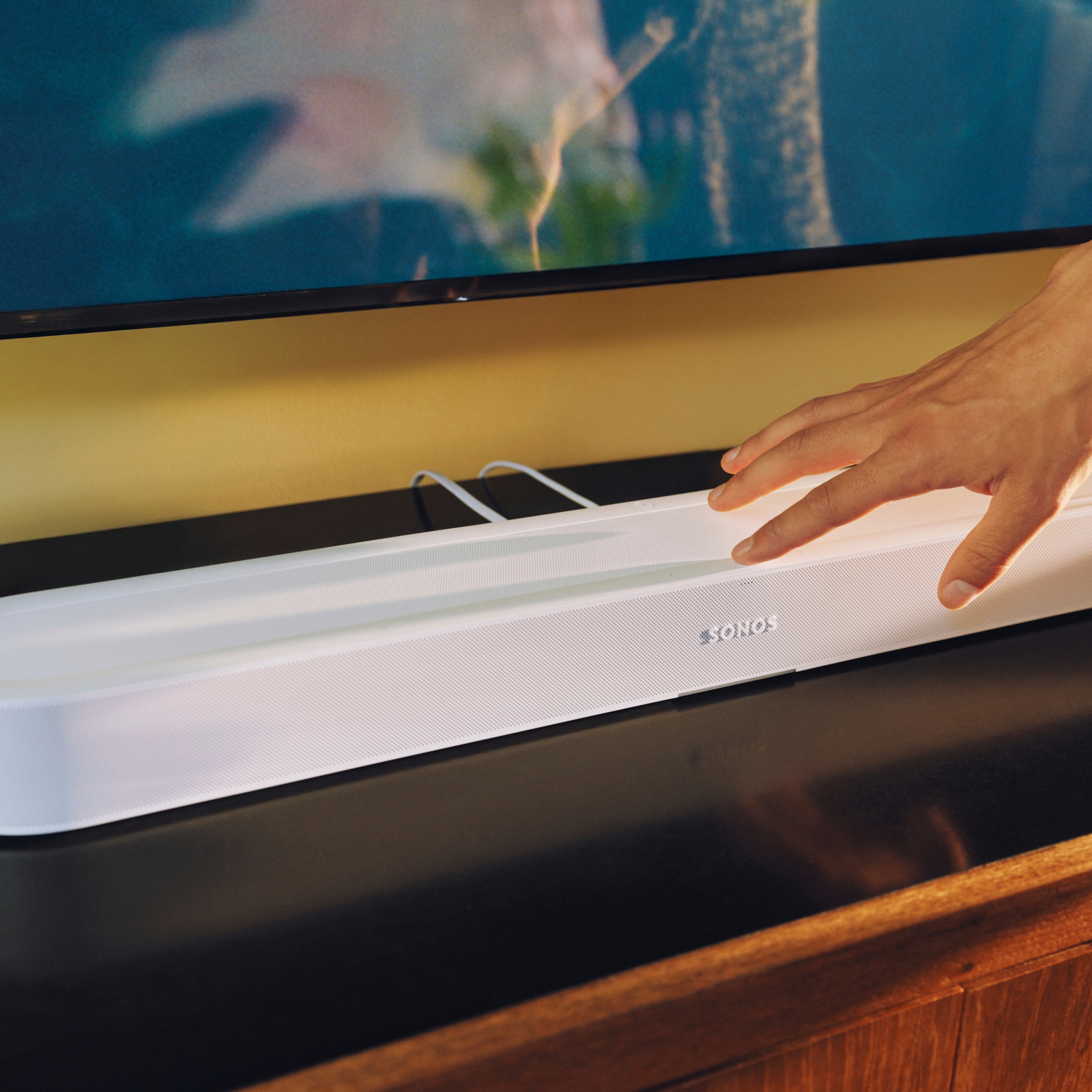 Close-up of a hand using the controls on a white Sonos Beam Ultra soundbar